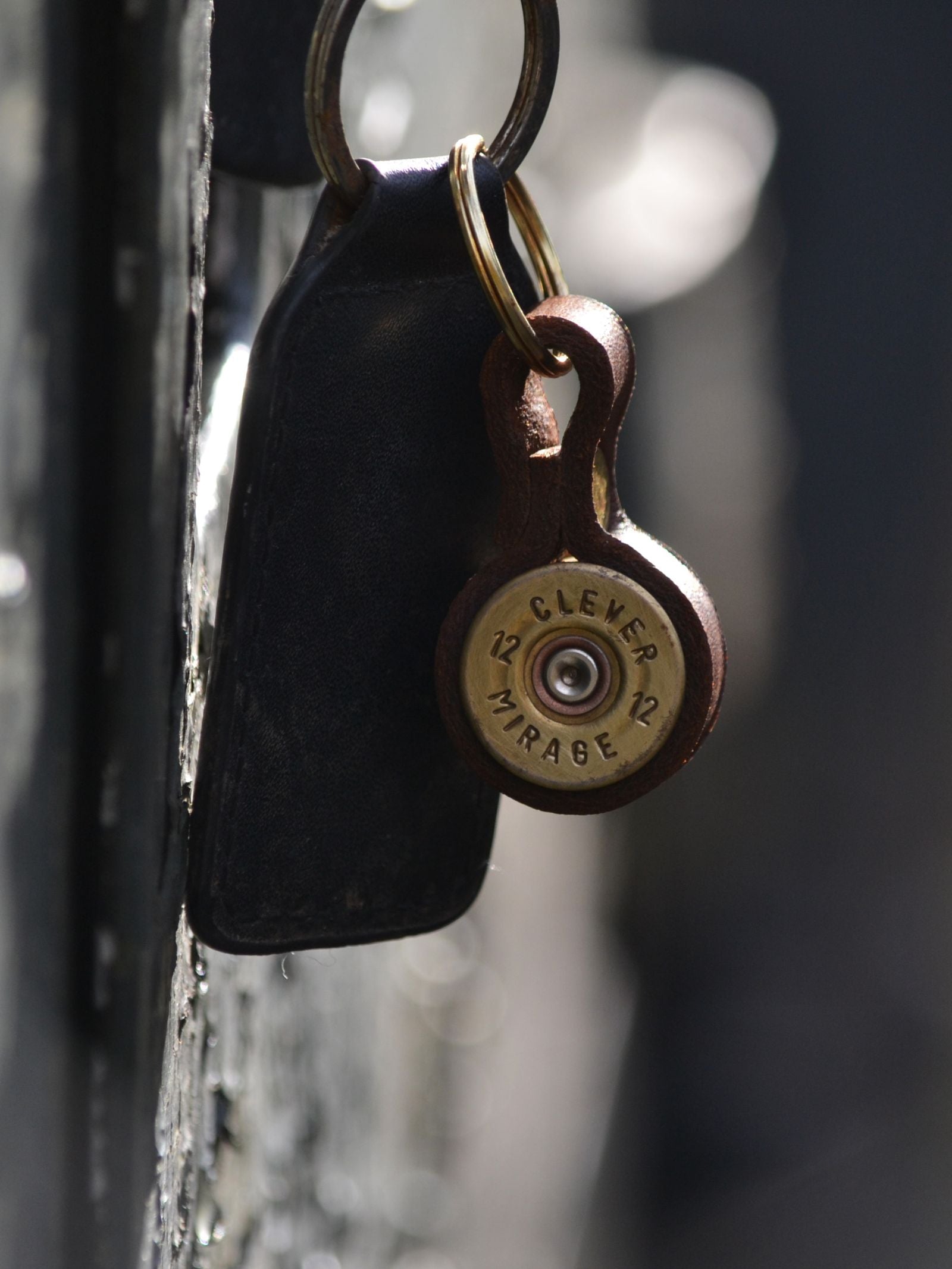 A close-up of the Cartridge Keyring by Campbell's of Beauly, shaped like a shotgun cartridge and attached to a dark leather key ring—an ideal gift for country sports enthusiasts.