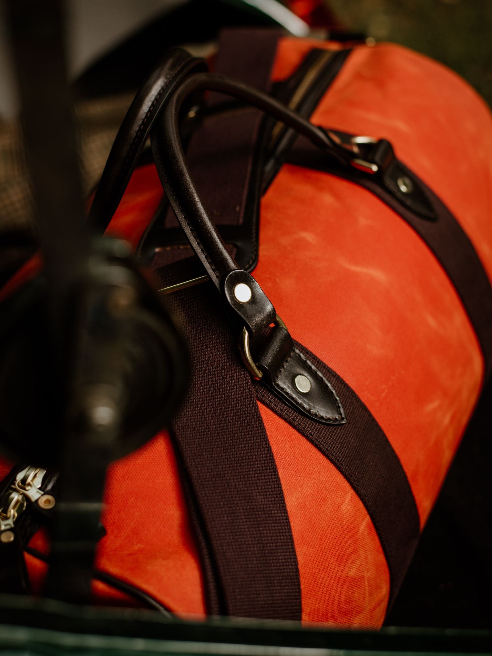 A close-up of the Campbell's of Beauly Wax Holdall, featuring orange waxed canvas, black straps, and bridle leather handles, resting in a car’s backseat.