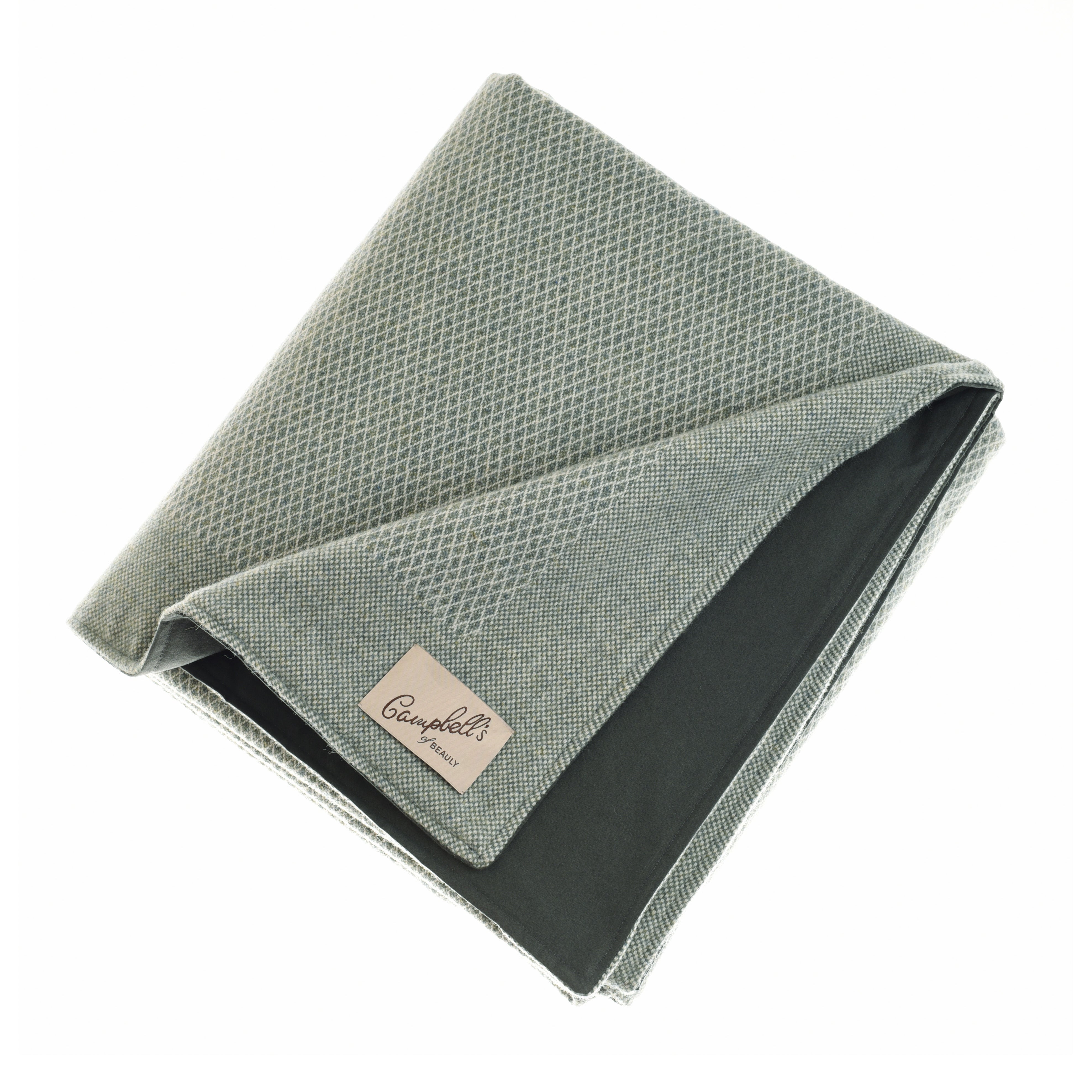 A folded, textured green Campbell’s of Beauly Waterproof Picnic Blanket with a dark underside is shown. A beige label reading “Campbell’s of Beauly” is stitched on one corner, all set against a white background.