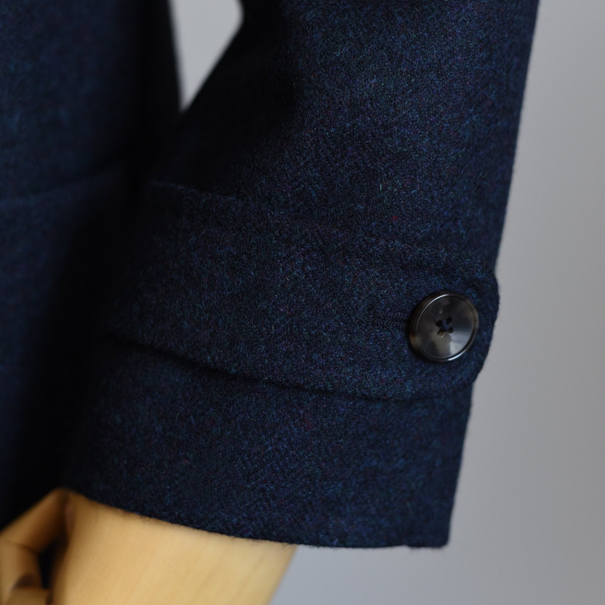Close-up of Campbells of Beauly Midnight Collar Coat sleeve in dark blue wool, featuring classic tailoring and a black button on a wooden mannequin arm against a plain backdrop.