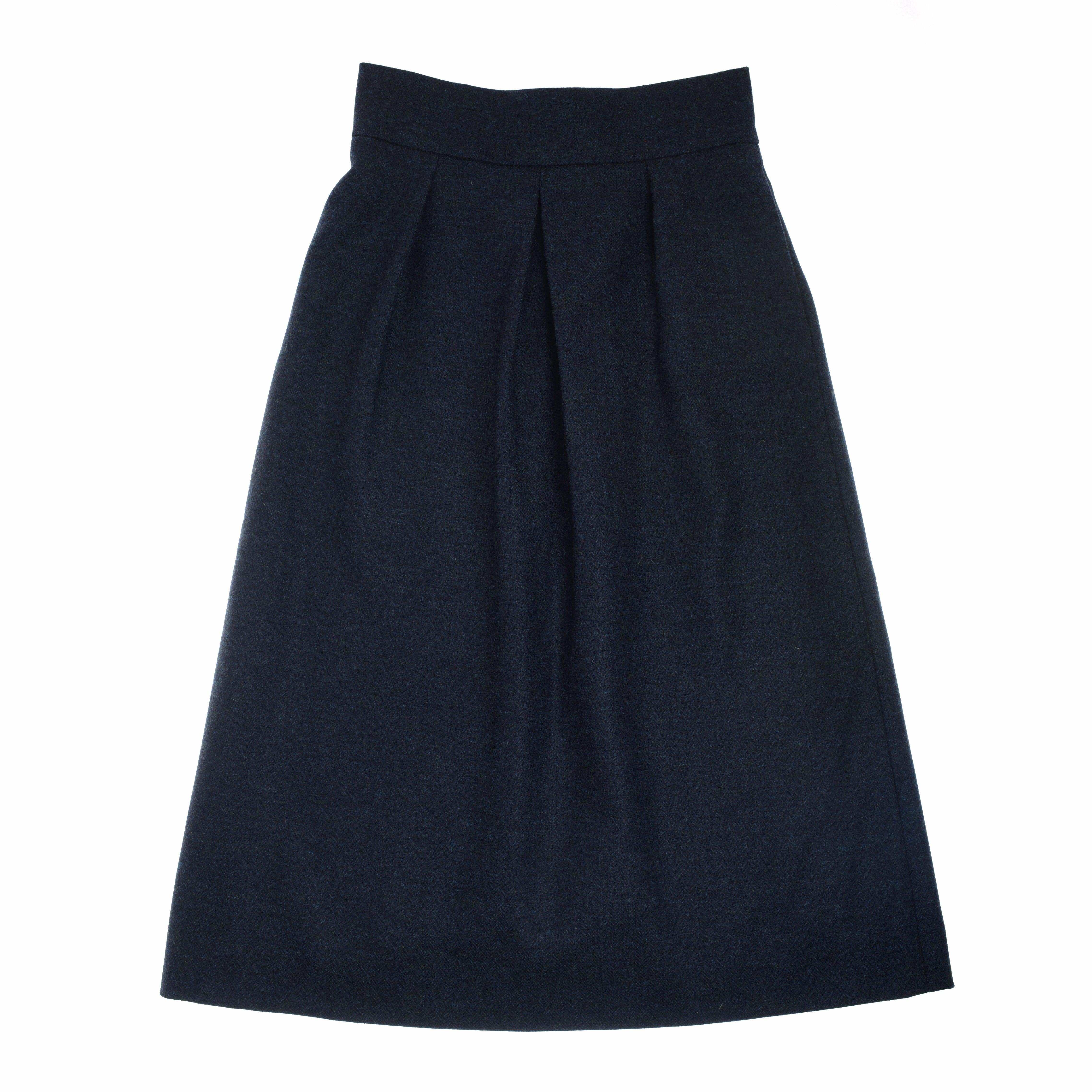 The Bell Skirt by Campbell’s of Beauly is a knee-length, midnight blue tweed skirt with a wide waistband and front pleats for a flared silhouette, shown laid flat on white. The smooth, medium-weight fabric suits formal or office wear.