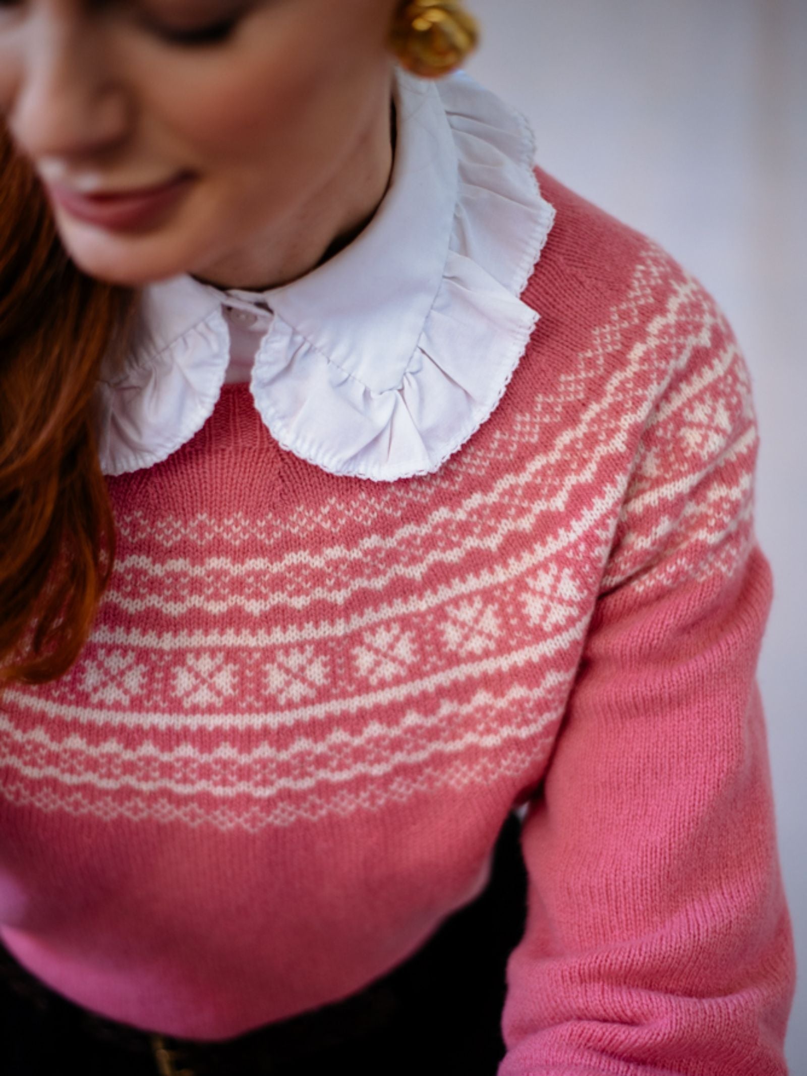 A woman with red hair wears Campbell’s of Beaulys Two-Colour Fairisle Yoke Jumper over a white ruffled-collar blouse. Only her lower face and upper torso are visible, and she appears to be smiling softly.