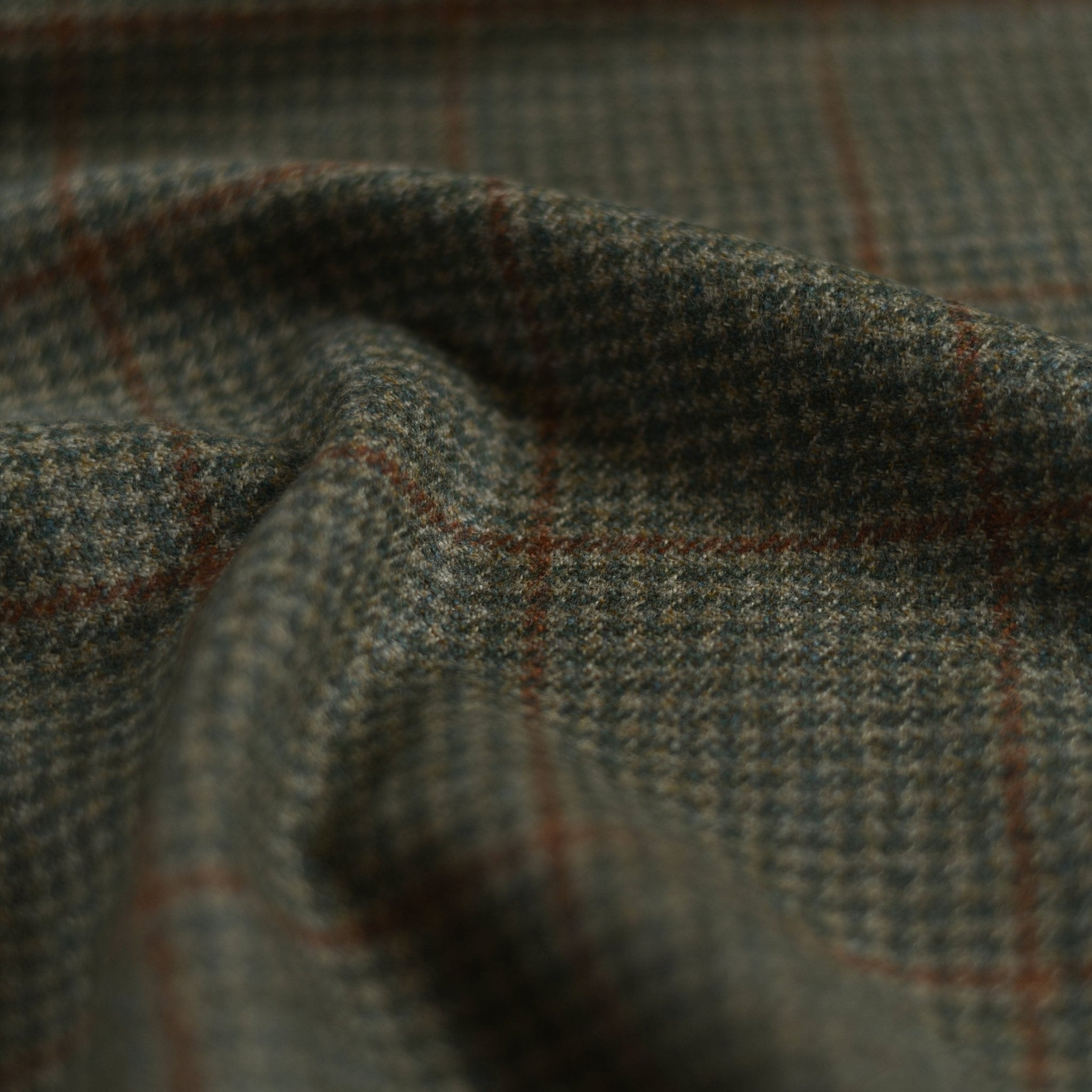 A close-up of Campbells of Beauly House Tweed 30199: heavyweight fabric with a green and brown houndstooth pattern, subtly accented by a reddish-brown windowpane check and a gently rumpled finish.