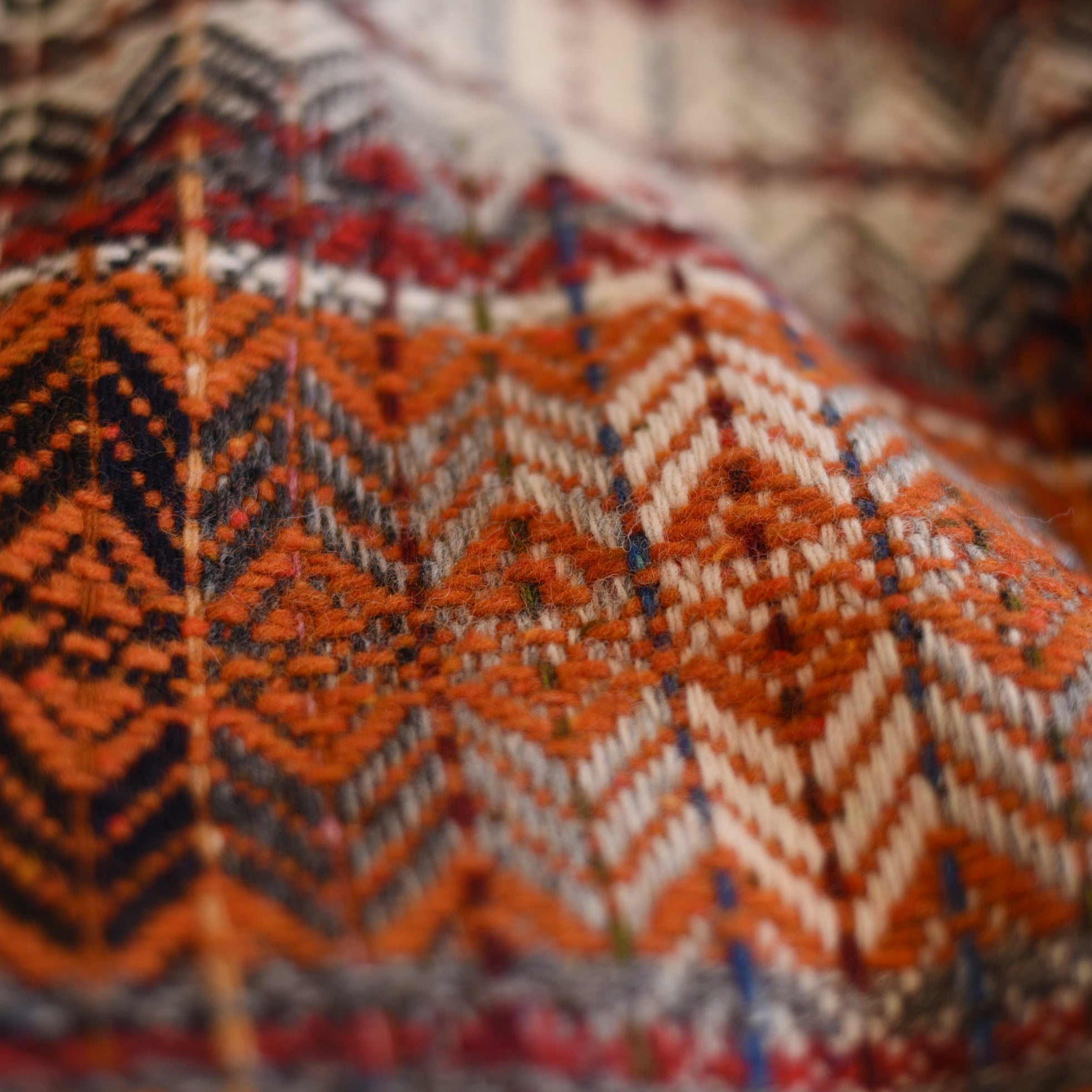 Close-up of the Campbell's of Beauly Auld Stock Wyvis Lambswool Throw, showcasing its colorful orange, red, navy, beige, and white zigzag geometric patterns, with visible yarn texture and a subtle diamond weave.