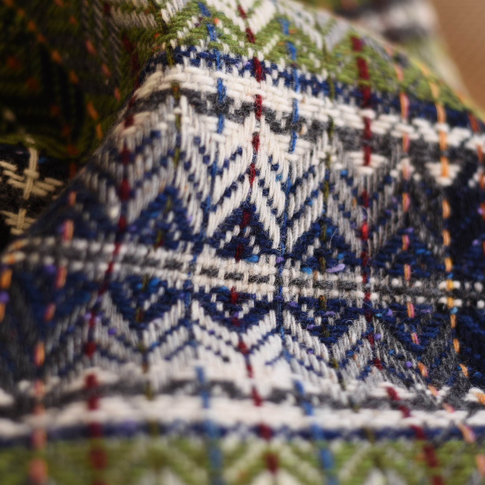 Close-up of the Wyvis Lambswool Throw by Campbells of Beauly, showcasing its colorful geometric patterns in blue, green, white, and black with flecks of red and yellow. The intricate diamond weave and detailed texture are clearly visible.