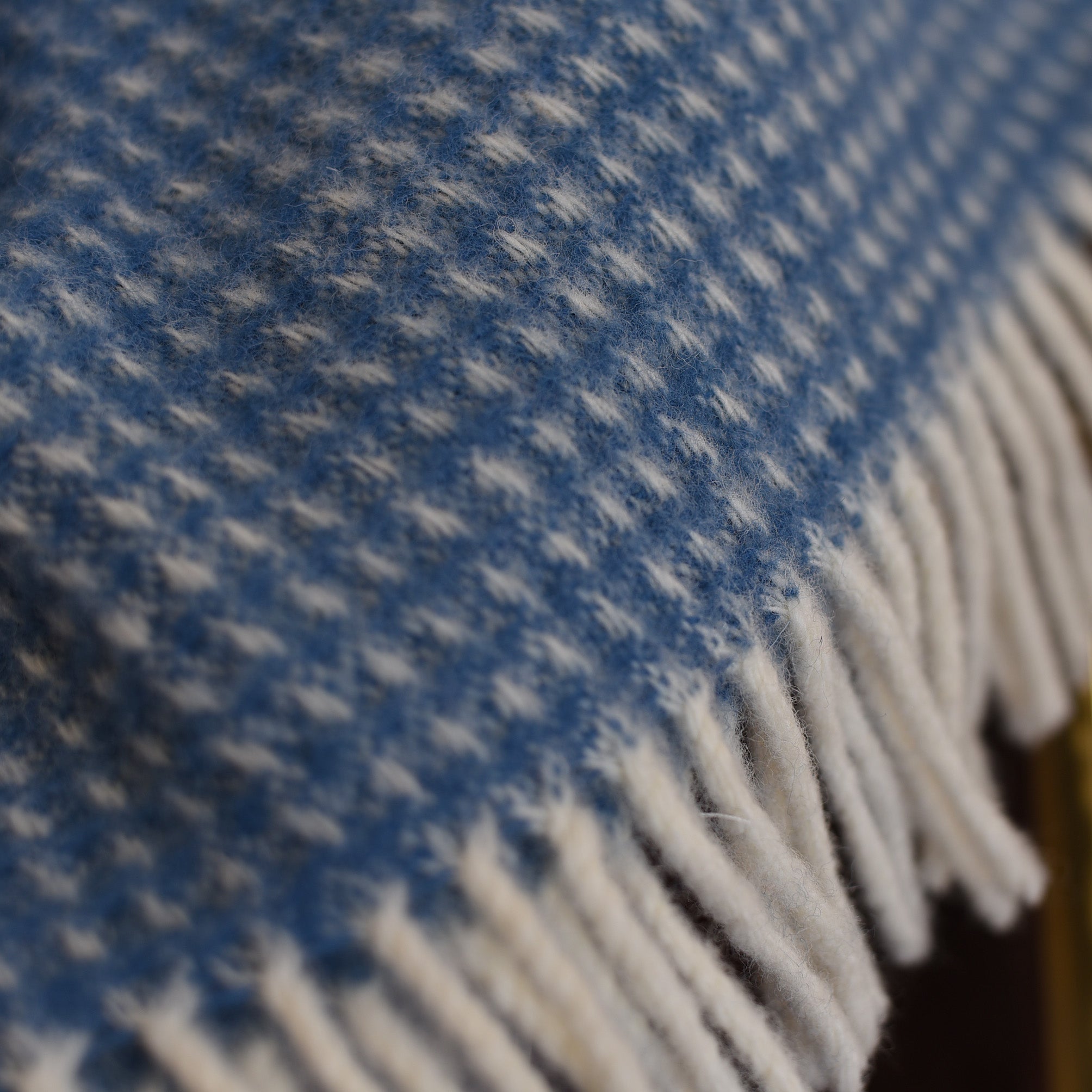 A close-up of the Campbells of Beauly Honeycomb Lambswool Throw, showcasing its blue and white pattern with soft white fringes along the edge.