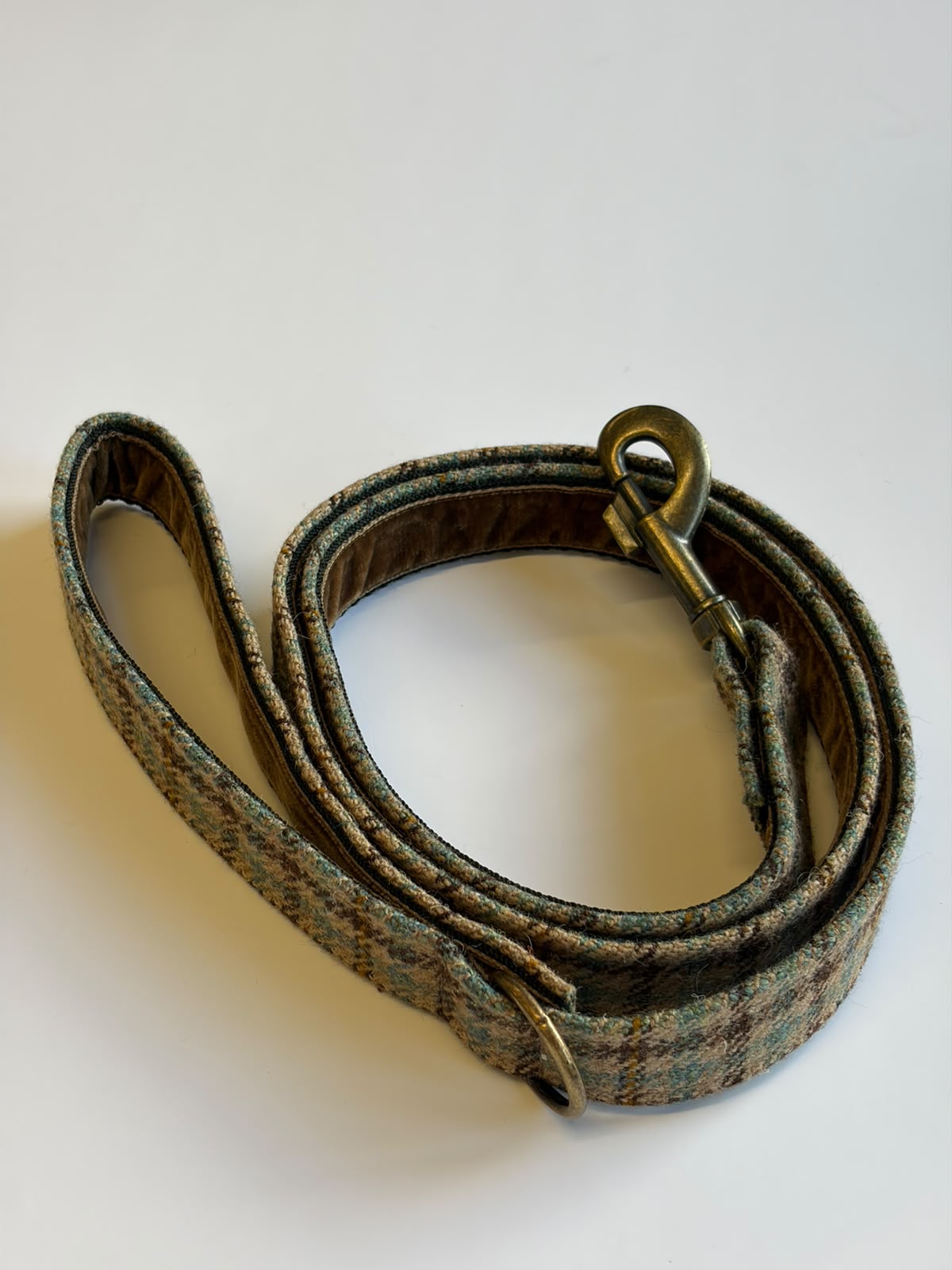 A coiled House Tweed Dog Lead by Campbell's of Beauly, crafted from plaid fabric and featuring a brass clip and metal ring, displayed on a white background.