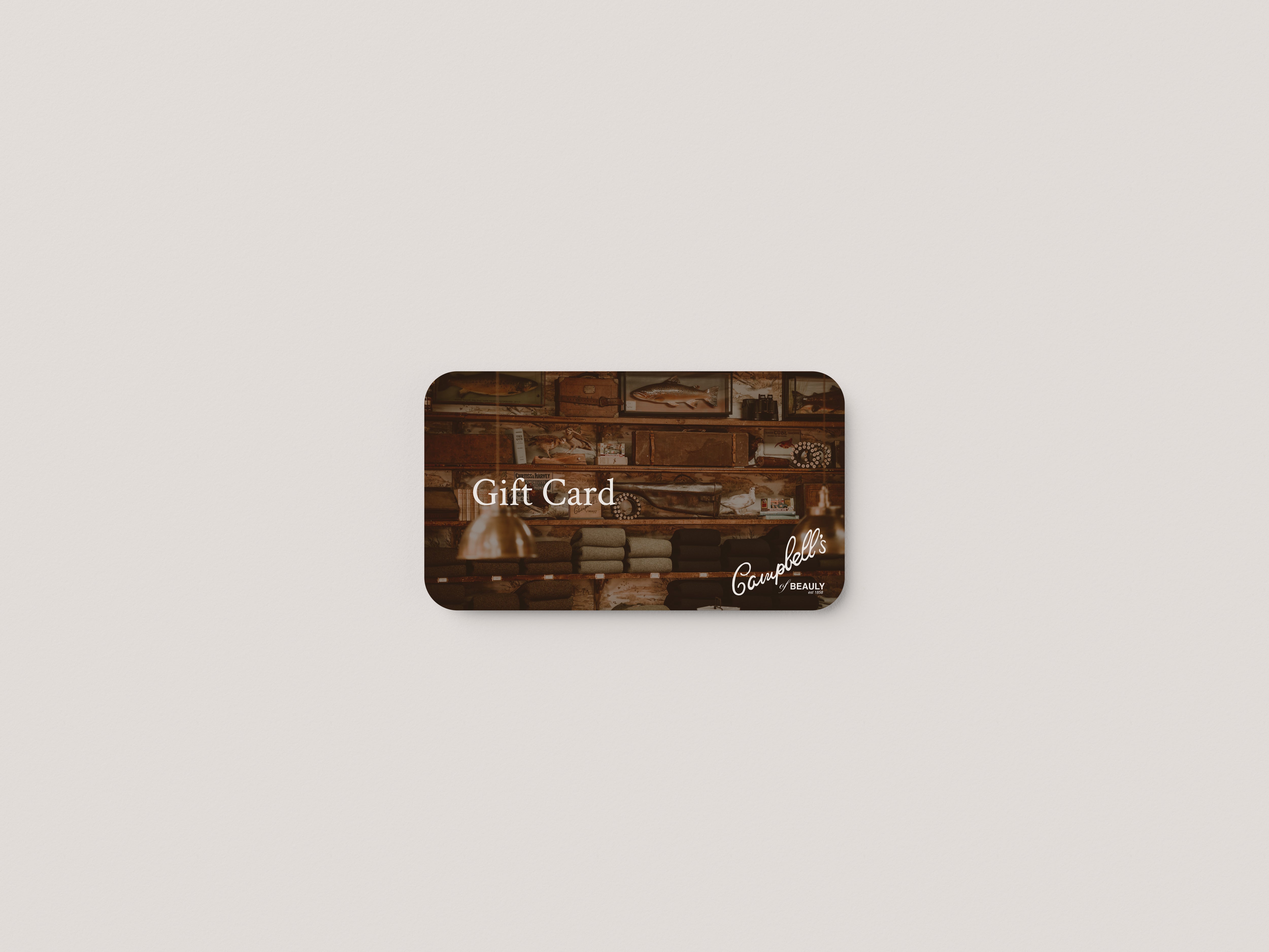 A rectangular Gift Card by Campbells of Beauly features a brown-toned background with shelves of items, Gift Card centered, and the brand’s cursive logo at the bottom right. The card rests on a white surface.