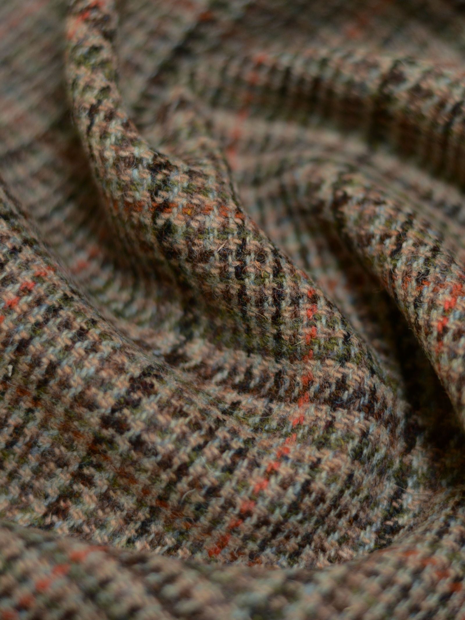 Close-up of House Tweed 93908 by Campbell's of Beauly, featuring a checkered pattern in muted brown, green, and orange tones. The softly draped fabric highlights its traditional Scottish weave and textured finish.