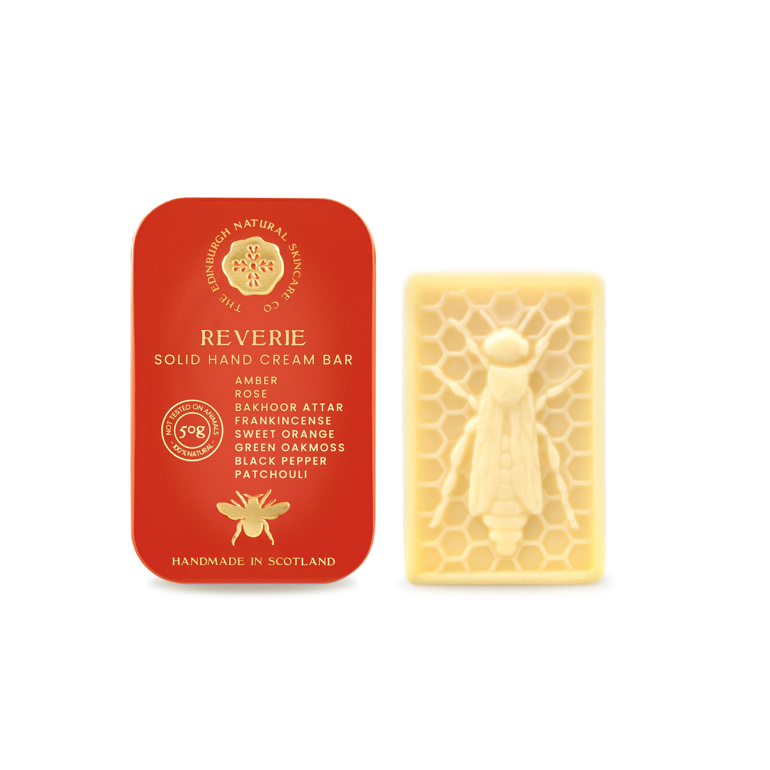 A red tin marked REVERIE by The Edinburgh Natural Skincare Company sits beside a pale yellow, cruelty-free hand cream bar with a bee on honeycomb. The handmade-in-Scotland tin displays gold text, a bee icon, and natural ingredients.