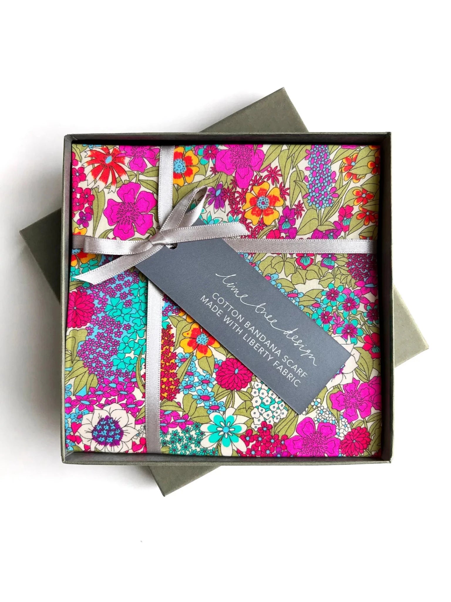 The Square Headscarf by Campbell's of Beauly in Ciara Lime features a vibrant floral pattern, boxed with a silver ribbon and gray tag reading "Cotton bandana scarf"—ideal as a neckerchief or pocket square, crafted with Liberty fabric.