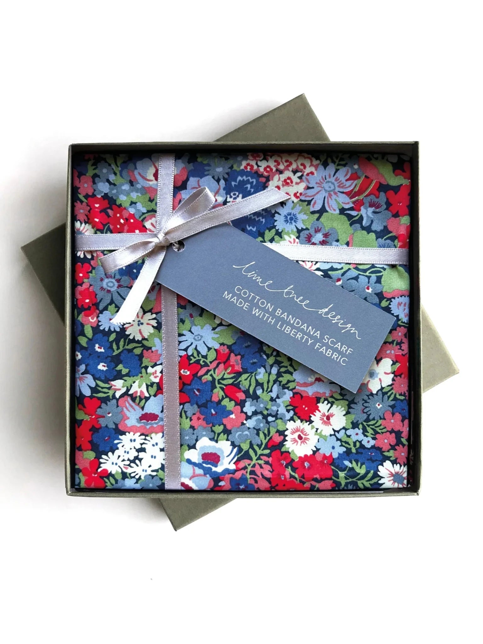 A Thrope-colored Square Headscarf by Campbell’s of Beauly, folded in a square gift box with a silver ribbon and blue tag reading, Cotton Bandana Scarf Made with Liberty Fabric; perfect as a neckerchief or pocket square.