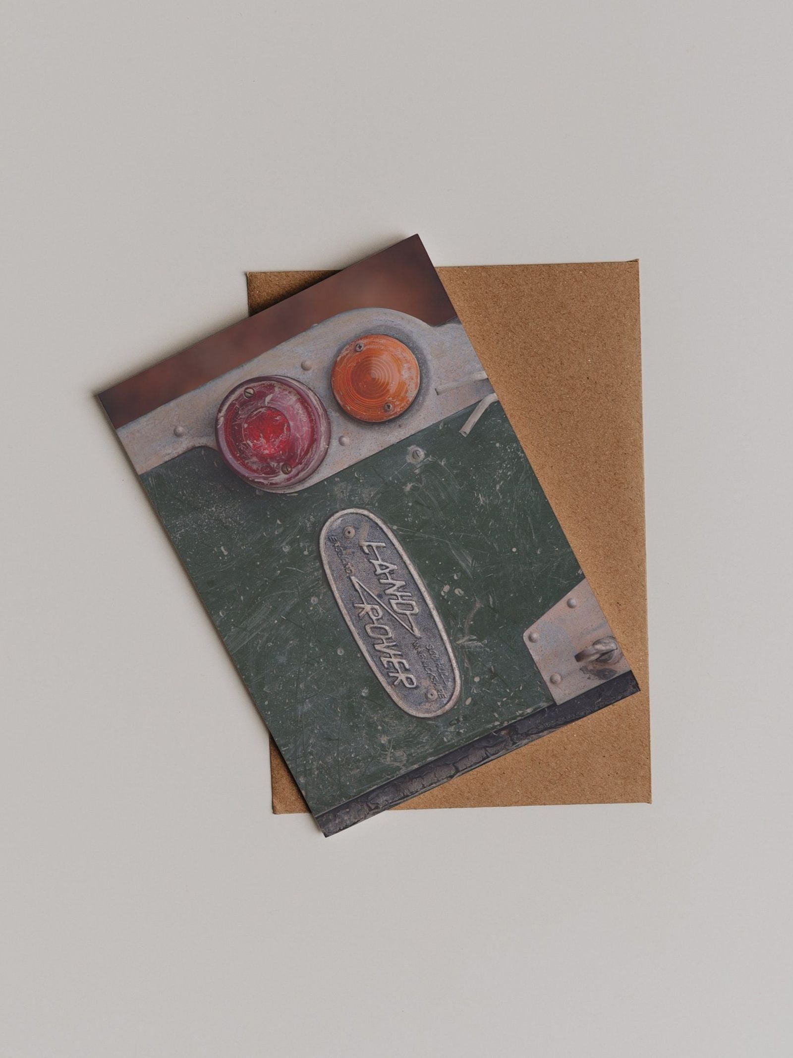 The Land Rover Defender Greeting Card by Campbell’s of Beauly features a photograph of vintage vehicle taillights with a metal plate reading LAND ROVER, designed by Sophie Murray, and is displayed atop a plain brown envelope.