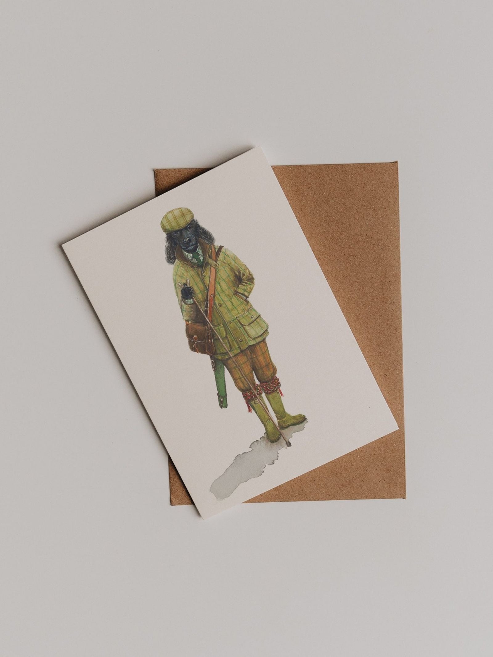 The Plus Fours Greeting Card by Campbell’s of Beauly features an illustration of a dog in vintage hunting attire, elegantly displayed atop a brown envelope on a light surface—a design inspired by the classic style of Campbell’s of Beauly.