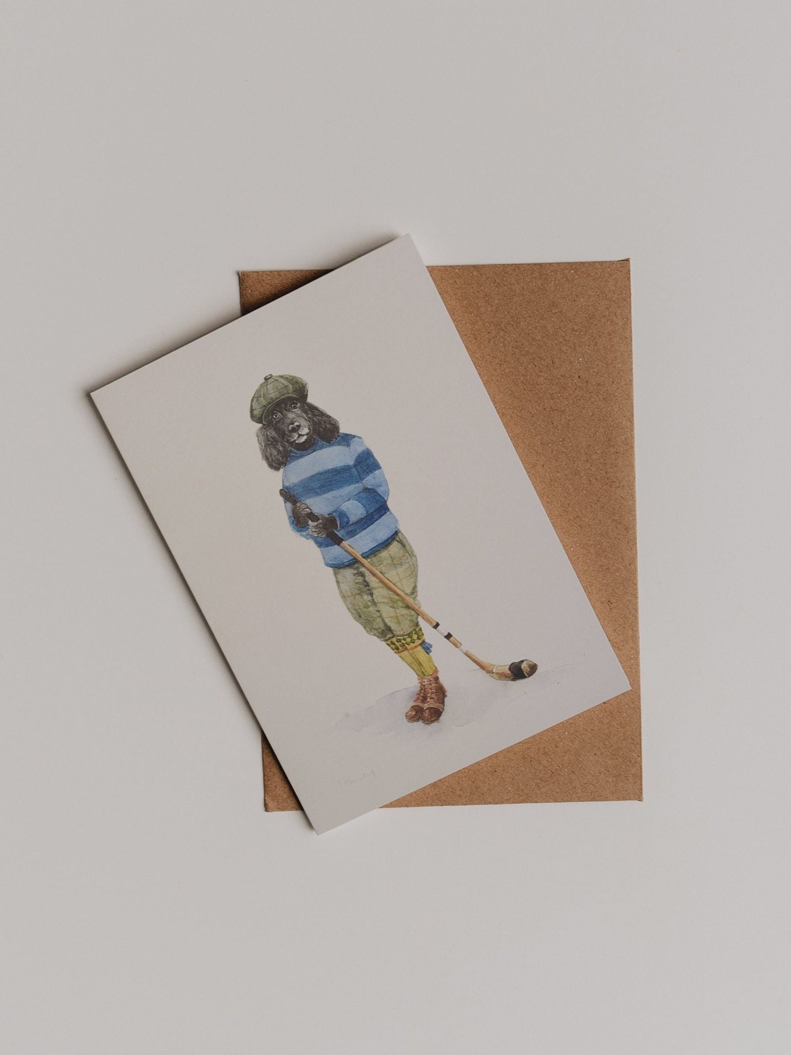 Here’s a rewritten version of your sentence using the provided product data: The Shinty Player Greeting Card by Campbell’s of Beauly, featuring an illustration inspired by classic sporting charm, is displayed on top of a brown envelope against a plain white background.
