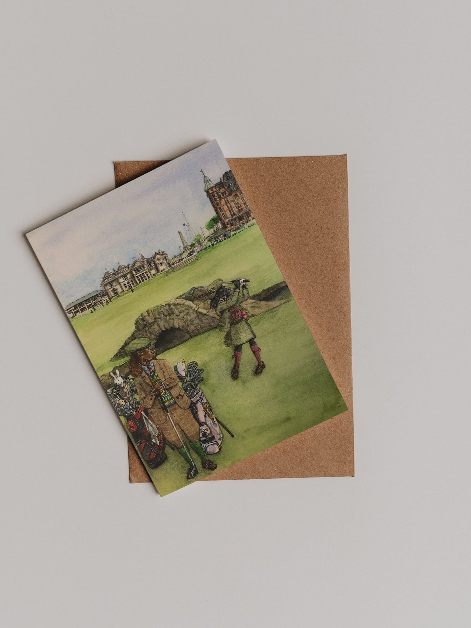 The St Andrews Swilken Bridge Greeting Card by Campbell’s of Beauly is shown atop a brown envelope against a plain white background.