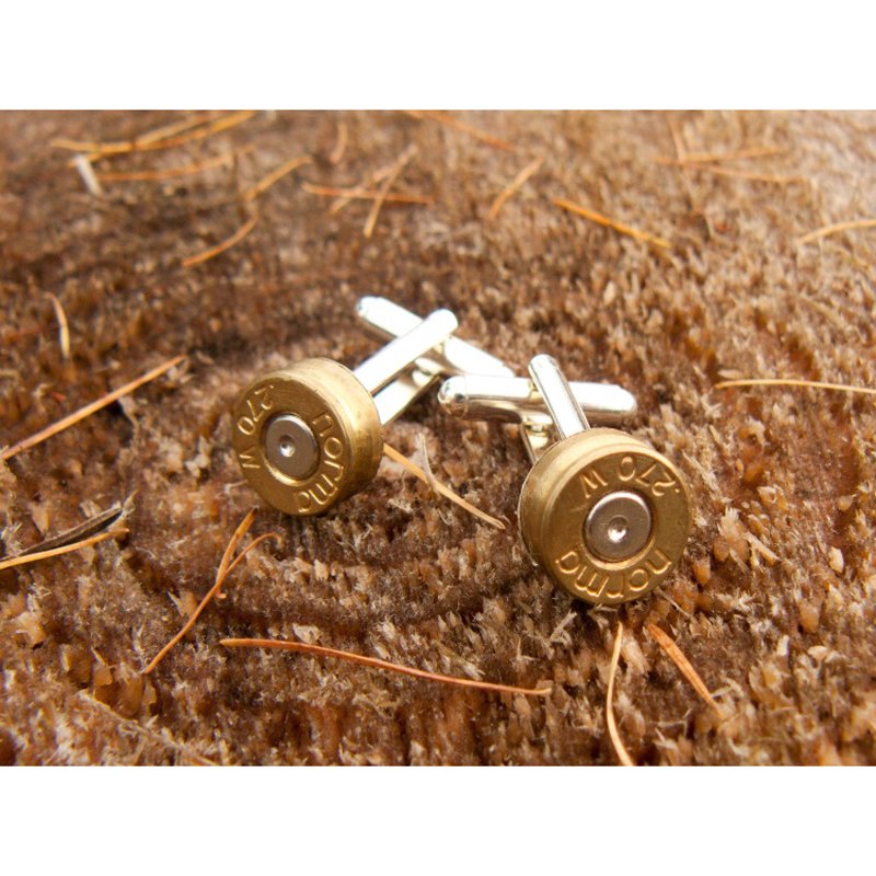 Campbells of Beauly Silver-Plated Bullet Cufflinks, crafted from recycled rifle bullets with Rottweil 270 W casing tops, rest on a brown textured surface dotted with dry pine needles—an ideal gift for shooting enthusiasts.