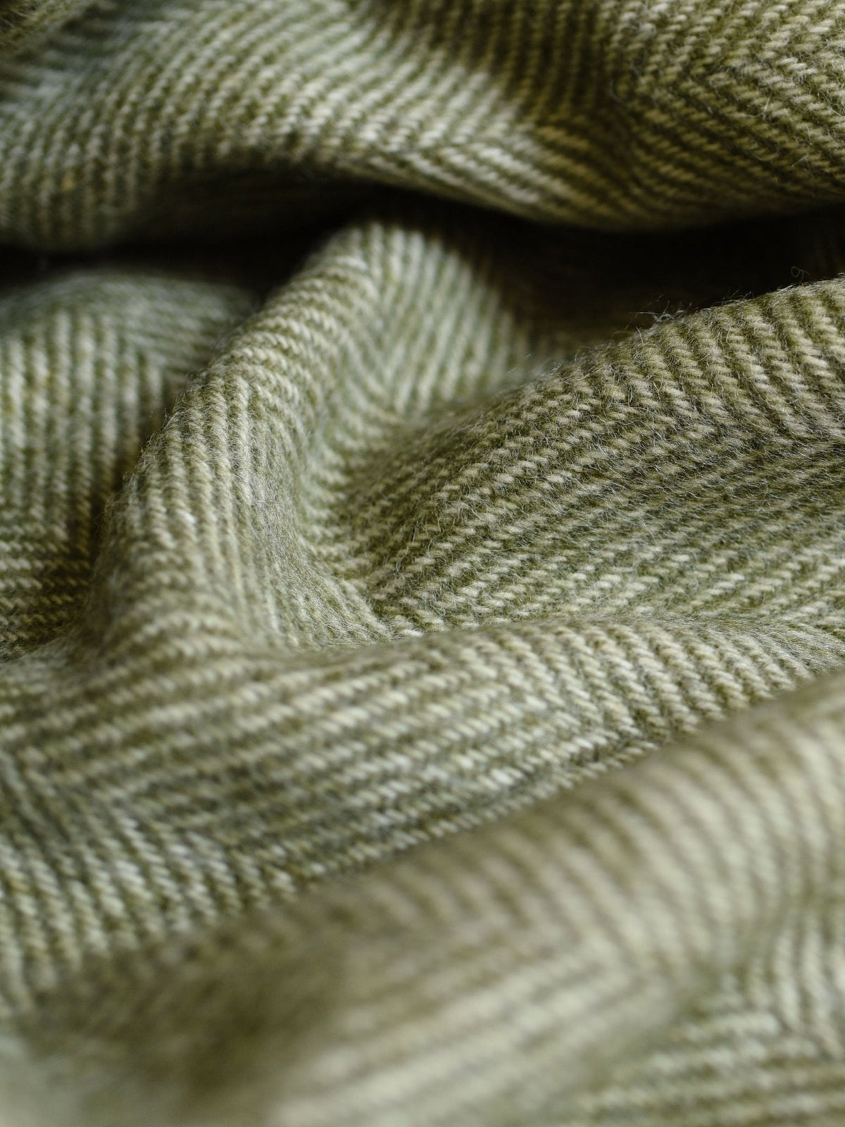 Close-up of green and beige herringbone patterned fabric with soft folds and a textured surface, expertly woven in Scotland by Campbell’s of Beauly for the British Wool Throw Green.