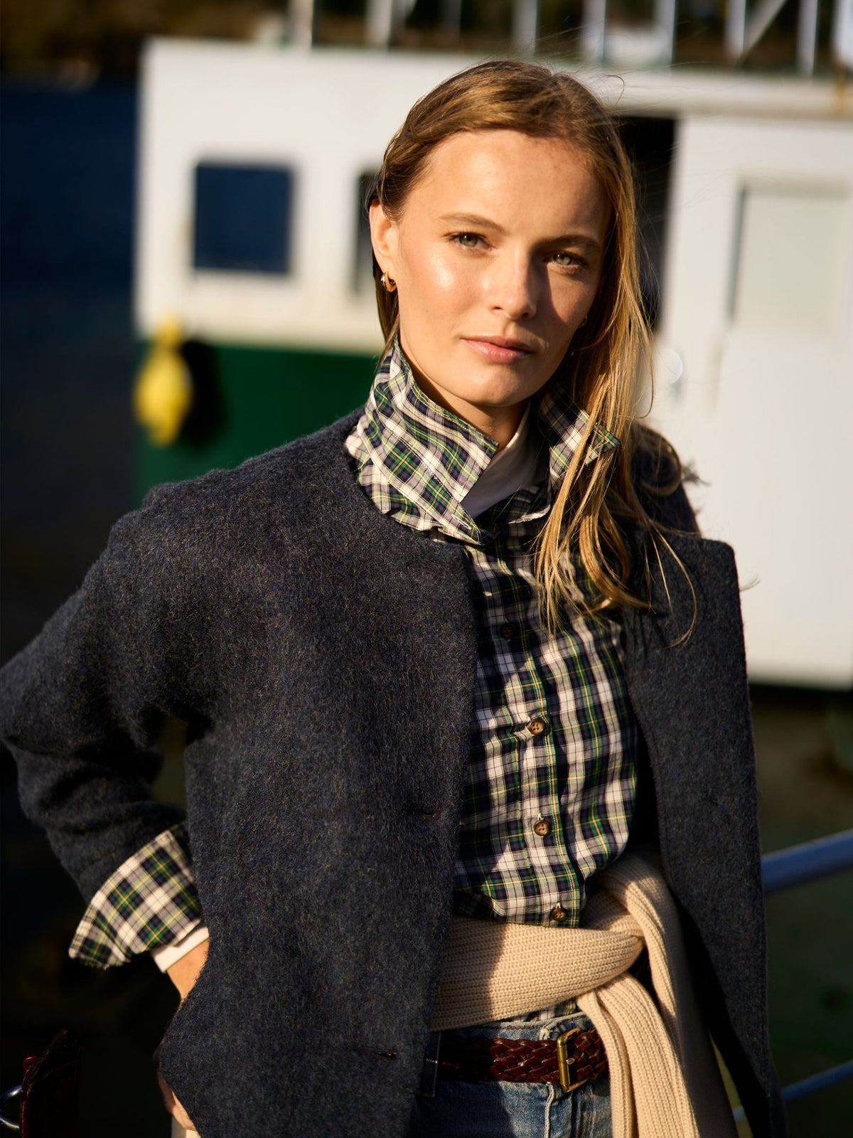 A woman wears a timeless, dark textured Campbell’s of Beauly Brushed Wool Jacket over a green and blue plaid collared shirt and a sweater tied around her waist.