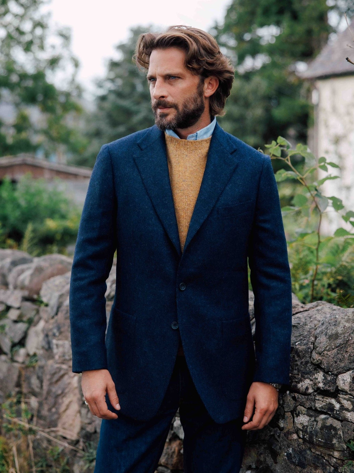 A man wears a navy blue Abraham Moon tweed Campbell’s House Jacket over a mustard yellow sweater and a light blue collared shirt.