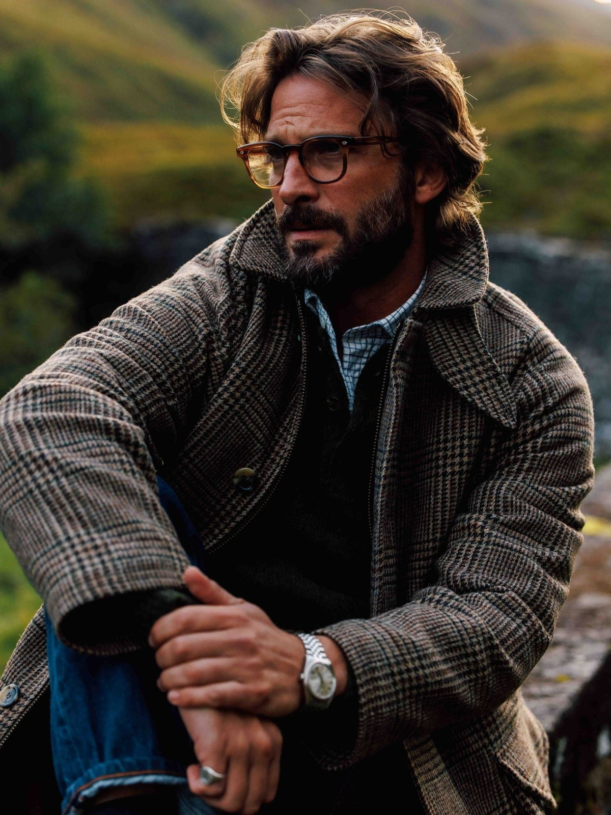 A bearded man wearing glasses in a brown patterned Cannich Coat by Campbell’s of Beauly over a dark sweater and blue shirt.