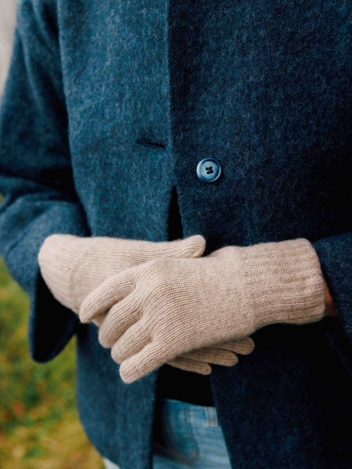 Hands wearing beige Campbell’s of Beauly cashmere gloves resting against a dark blue coat.
