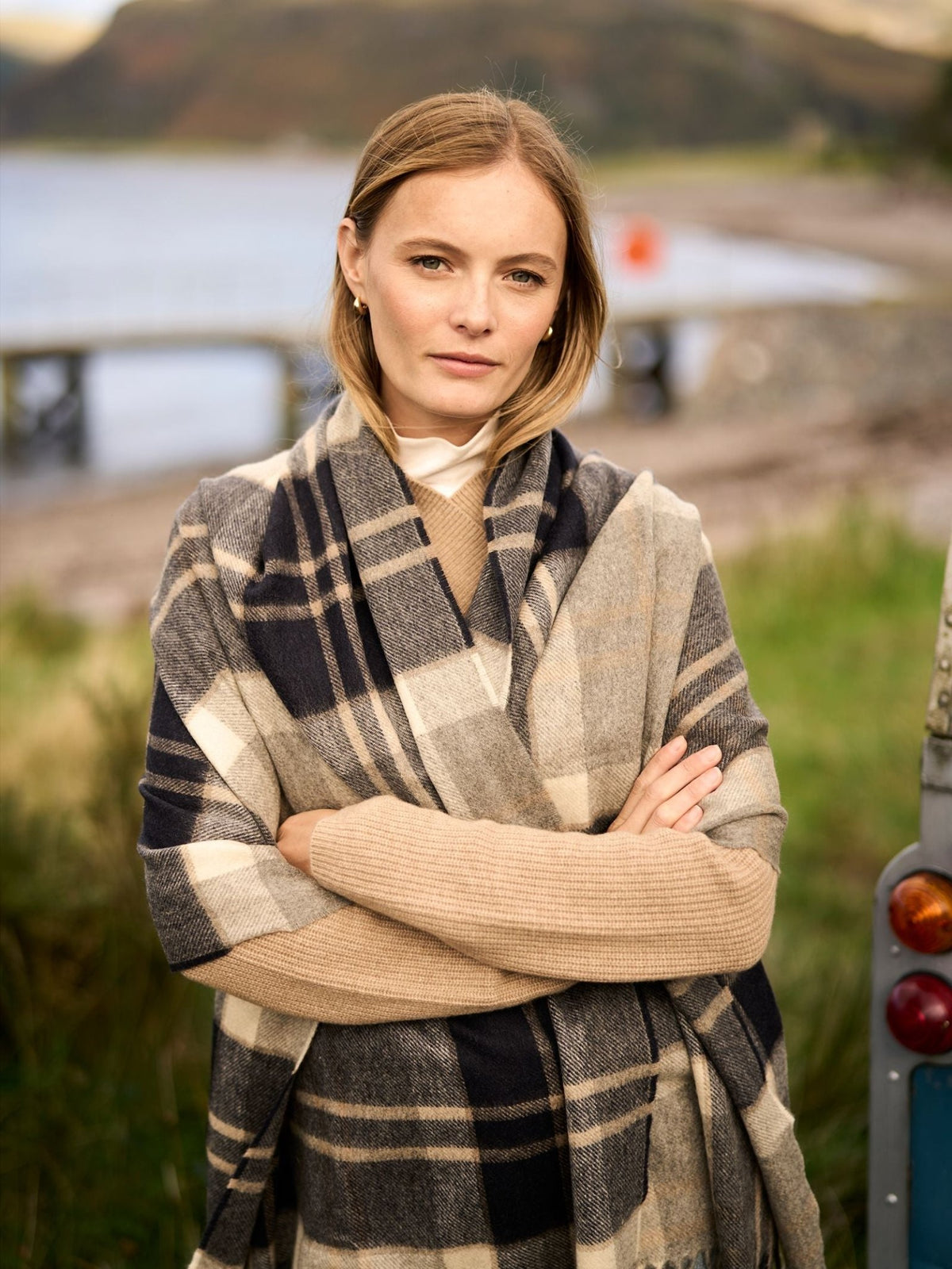 A woman wearing a tan sweater and a large, folded beige and navy blue Campbell’s of Beauly Cashmere Stole wrapped around her shoulders.