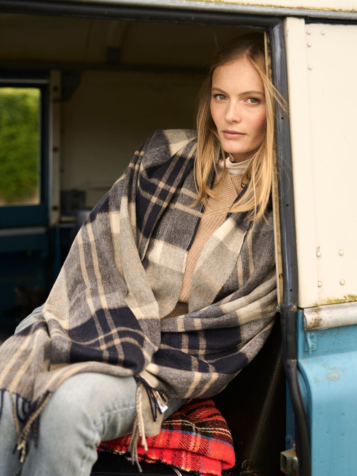 A woman sits inside a vehicle wearing a large, navy and beige Scottish Campbell’s of Beauly Cashmere Stole draped over her shoulders.