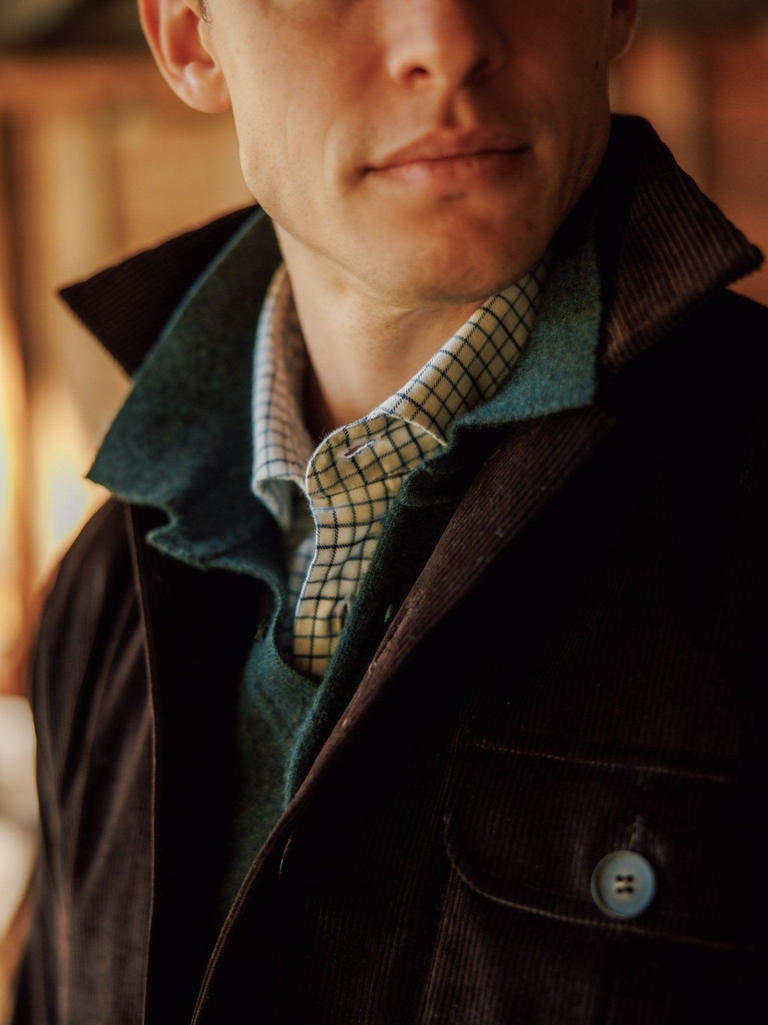 A person wearing the Casual Shacket by Campbell’s of Beauly—a dark cotton corduroy jacket with the collar turned up—layered over a green sweater and checkered shirt, photographed from the shoulders up in soft indoor lighting.