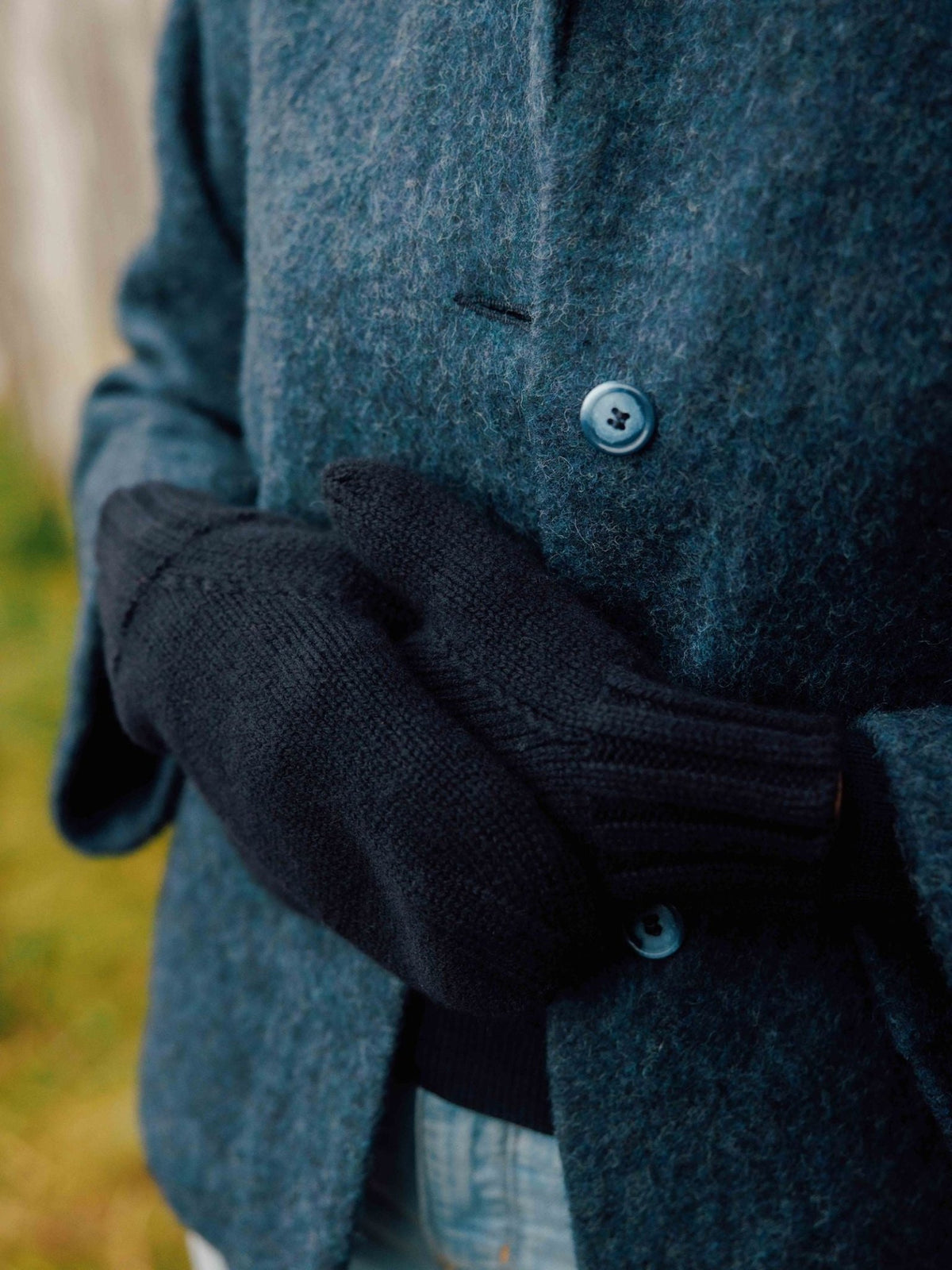 A person wearing black lambswool Chunky Mittens and a dark blue wool coat.