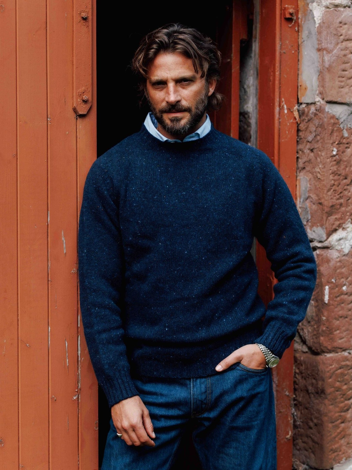 A man wearing a navy blue Donegal Lambswool Crew Neck Jumper by Campbell’s of Beauly over a light blue collared shirt.