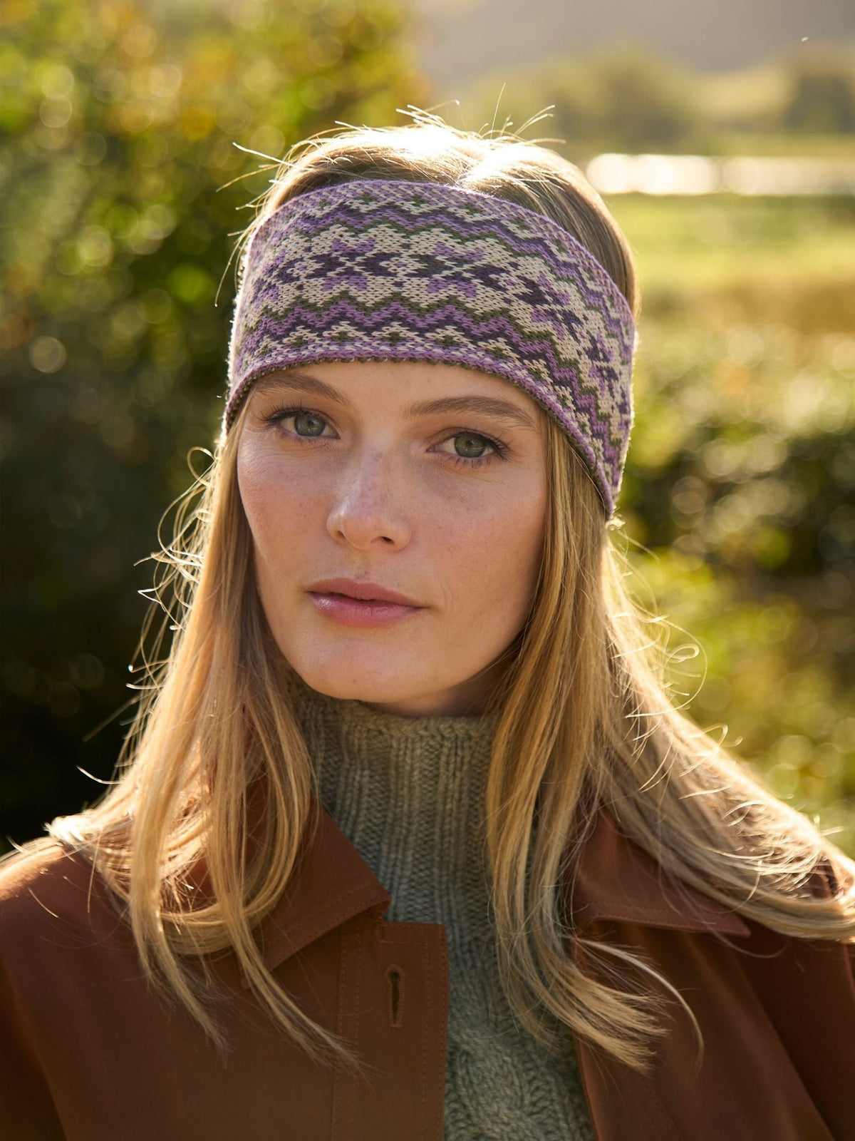 A woman wears a 100% wool Campbell’s of Beauly Fairisle headband in purple, green, and cream.