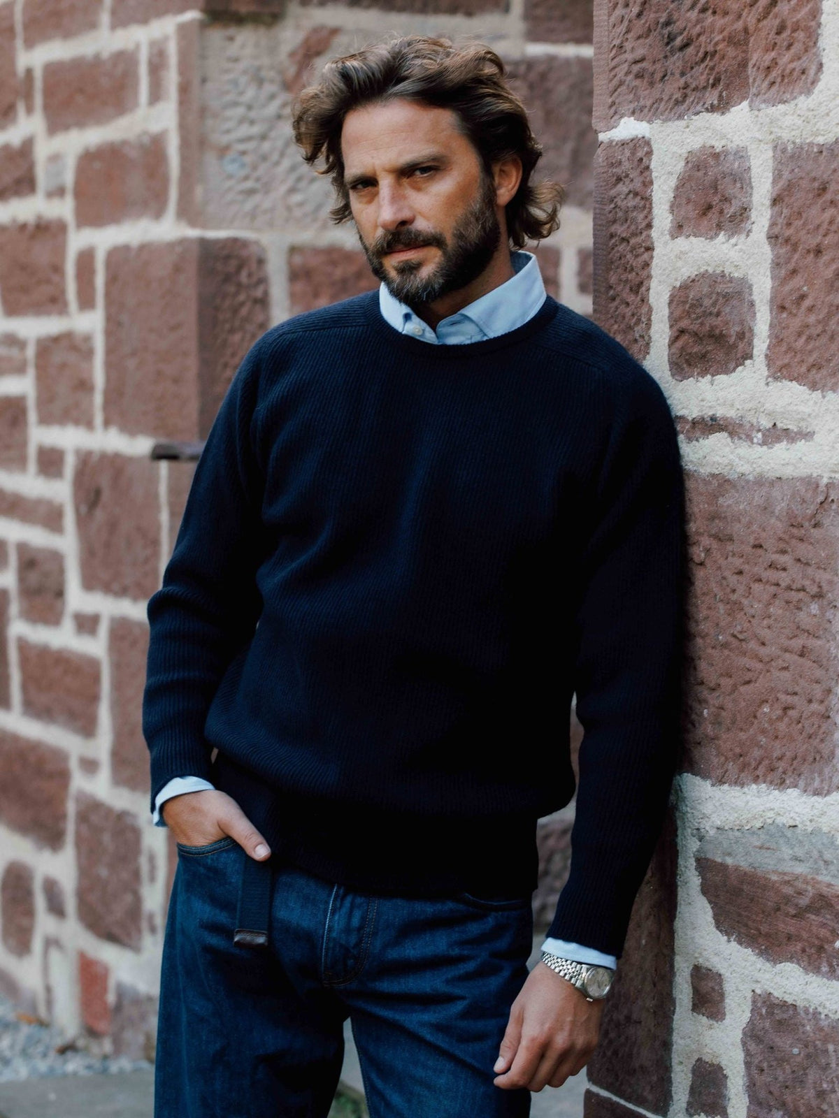A man wearing a navy blue Fisherman’s Rib Crew Jumper by Campbell’s of Beauly over a light blue collared shirt.