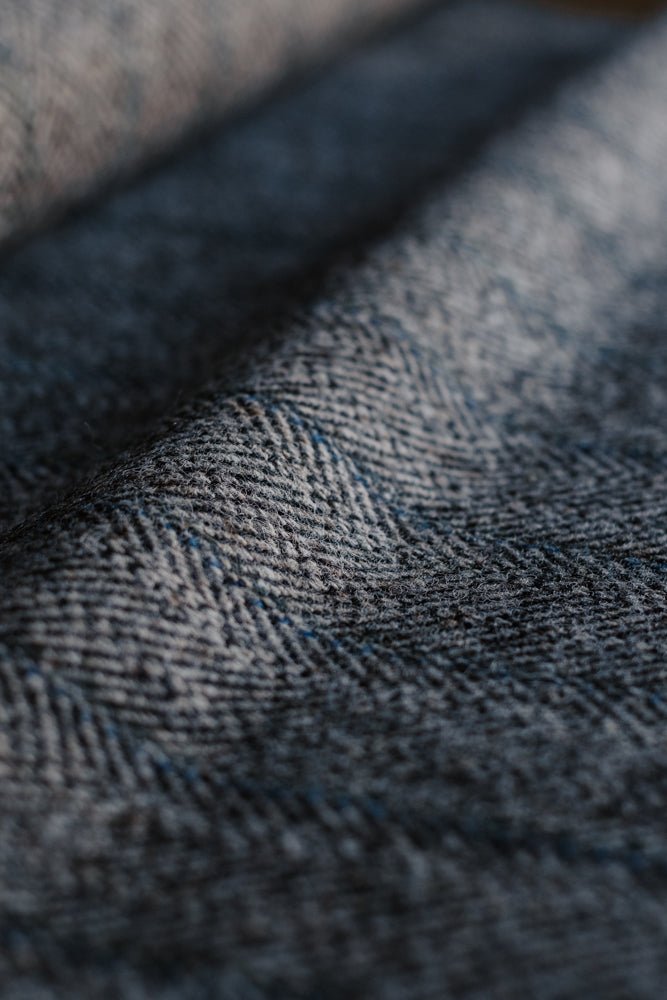 Close-up of Campbell’s of Beauly House Tweed 95053, featuring blue and gray herringbone patterned fabric with soft lighting and visible texture that highlights the detailed weave and subtle color variations characteristic of classic jacketing cloth.
