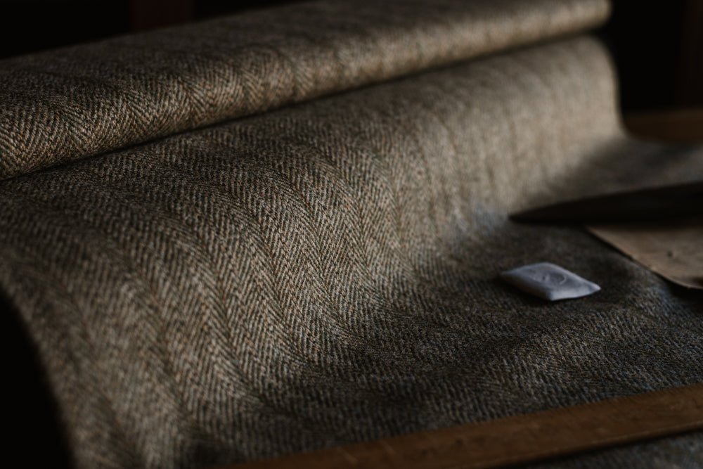 A close-up of a roll of Campbell’s of Beauly House Tweed 95054 fabric on a table, accompanied by a ruler, tailor’s chalk, and brown paper nearby, all softly side-lit—a timeless setting for crafting fine jacketing cloth.