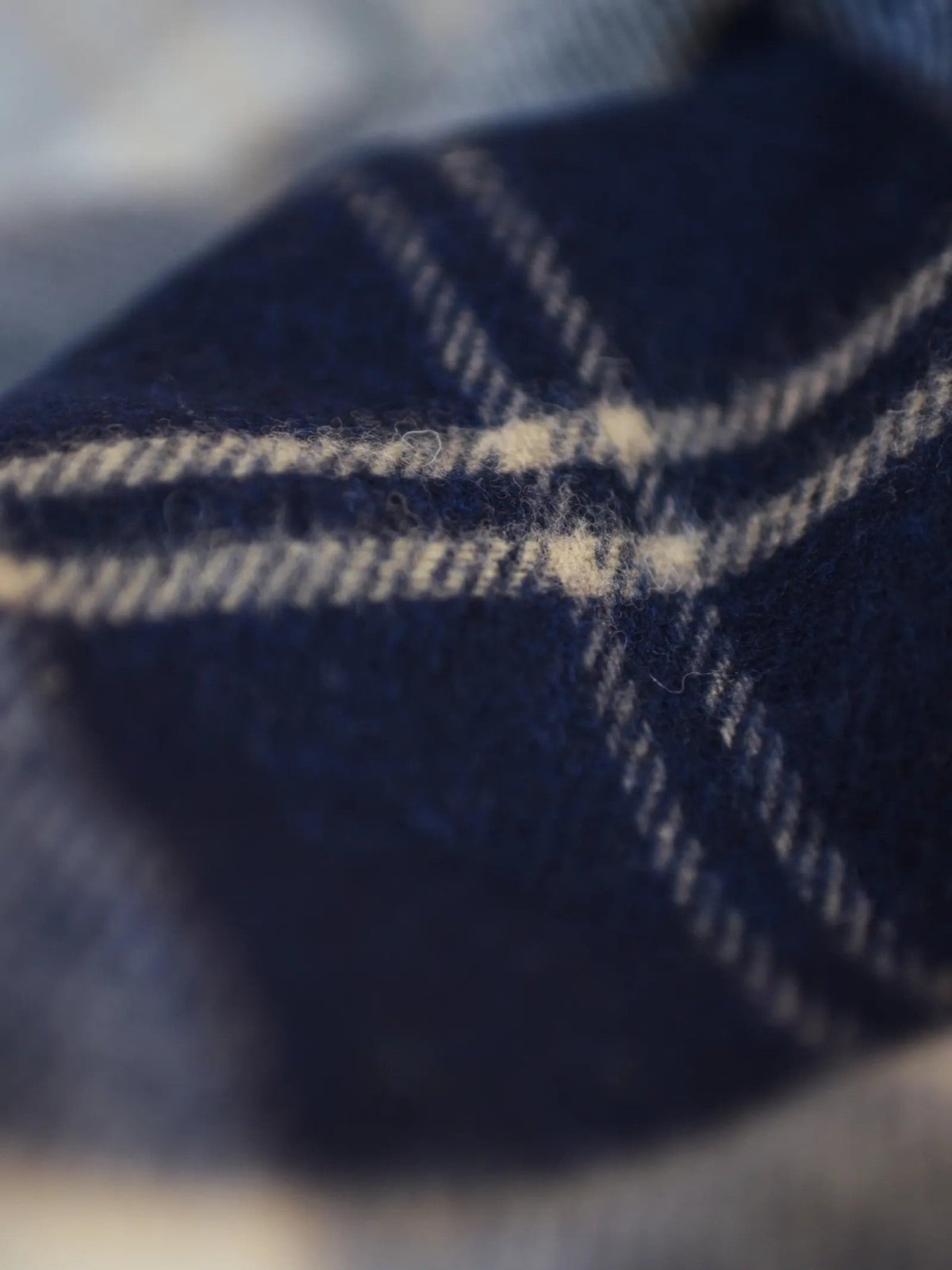 Close-up of a soft, fuzzy fabric featuring a navy blue and cream plaid pattern, highlighting the detailed texture and intersecting lines—an exquisite example of the Lambswool Tartan Blanket by Campbell’s of Beauly, expertly crafted in the UK and rich with heritage charm.