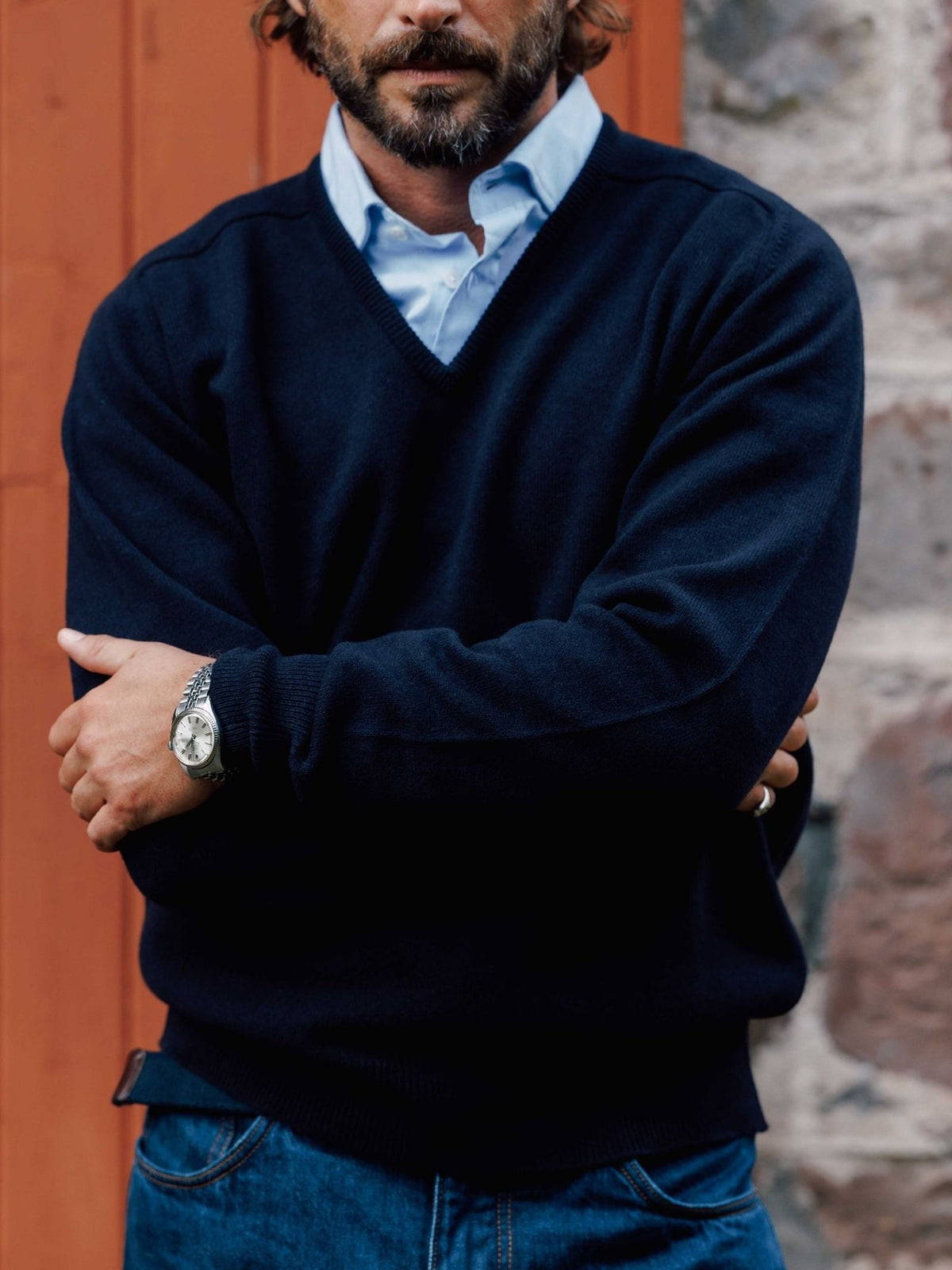 A man with his arms crossed wearing a classic-fit Campbell’s of Beauly Lambswool V-Neck Jumper over a light blue button-down shirt.
