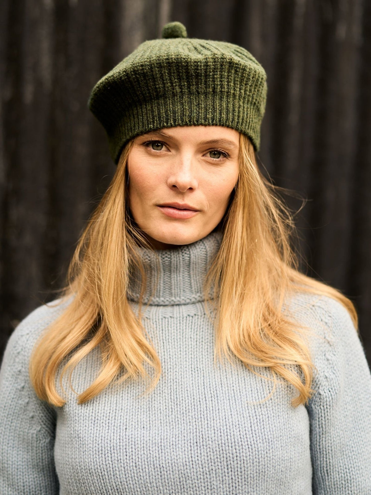 A woman wears a green Rib Beret by Campbell’s of Beauly with a light blue turtleneck sweater in winter wear.