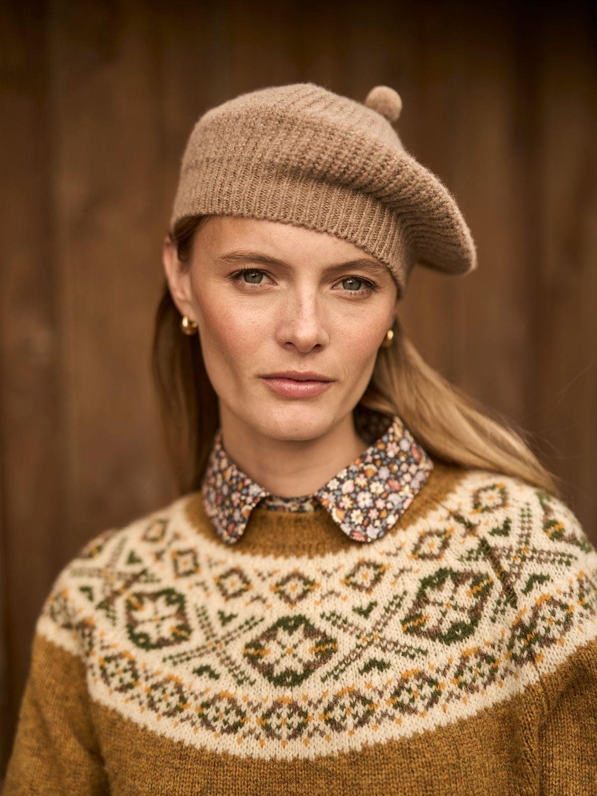 A person in cozy winter wear, featuring a tan ribbed knit Rib Beret with a small pom-pom and a patterned Fair Isle sweater.