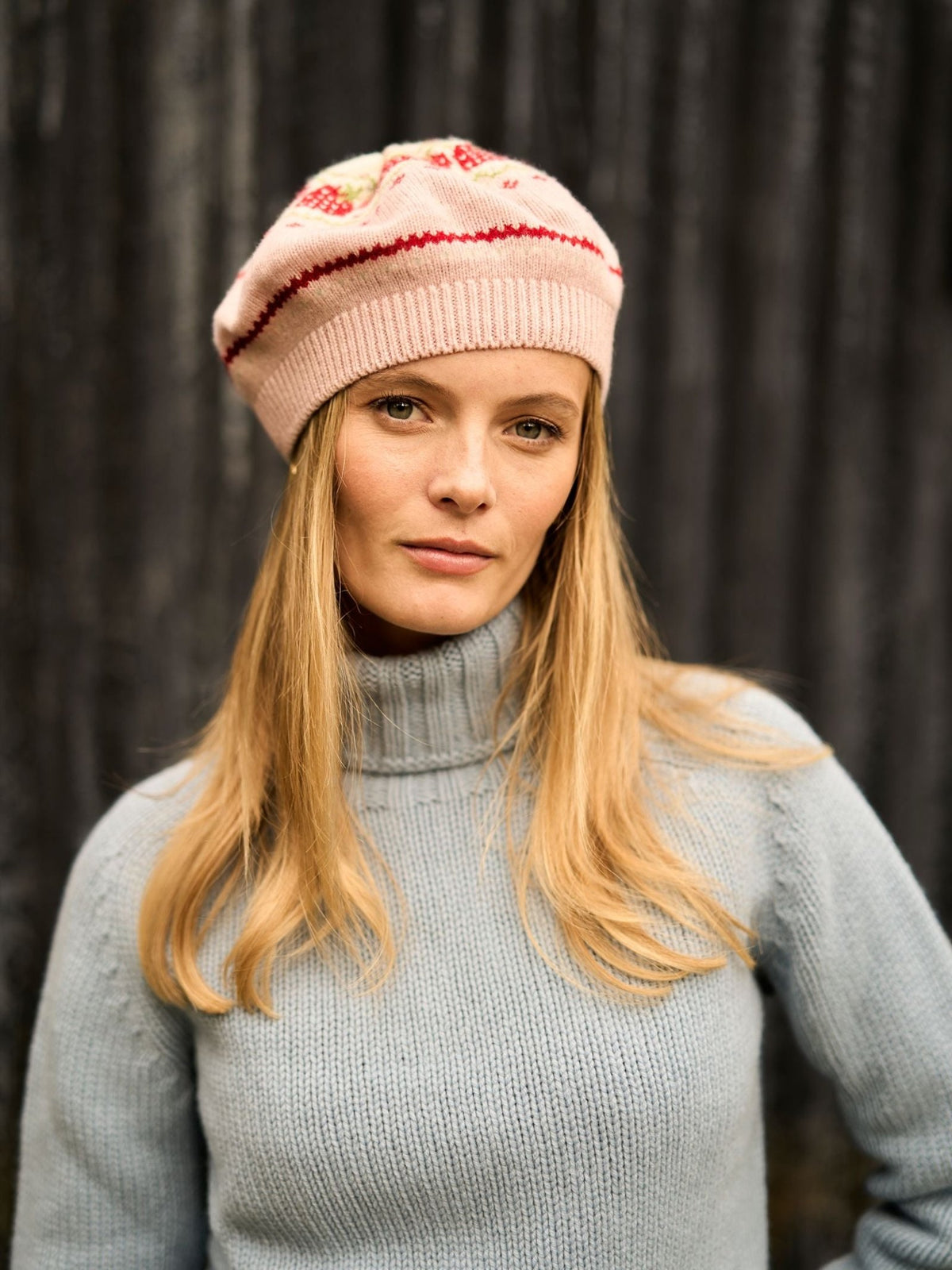 A woman wearing a pale pink Campbell’s of Beauly Strawberry Beret featuring a red stripe and a strawberry design.