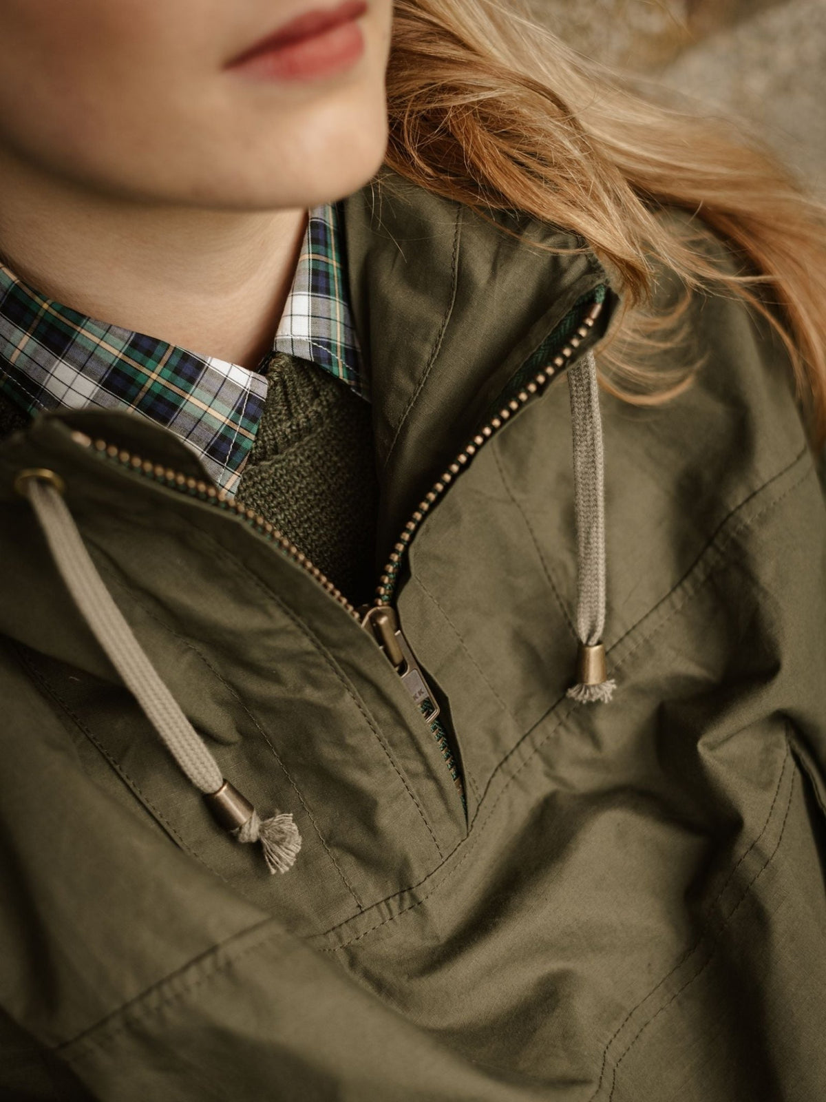 Olive green dry wax ripstop hooded Stalker Smock worn over a plaid collared shirt and a green sweater.