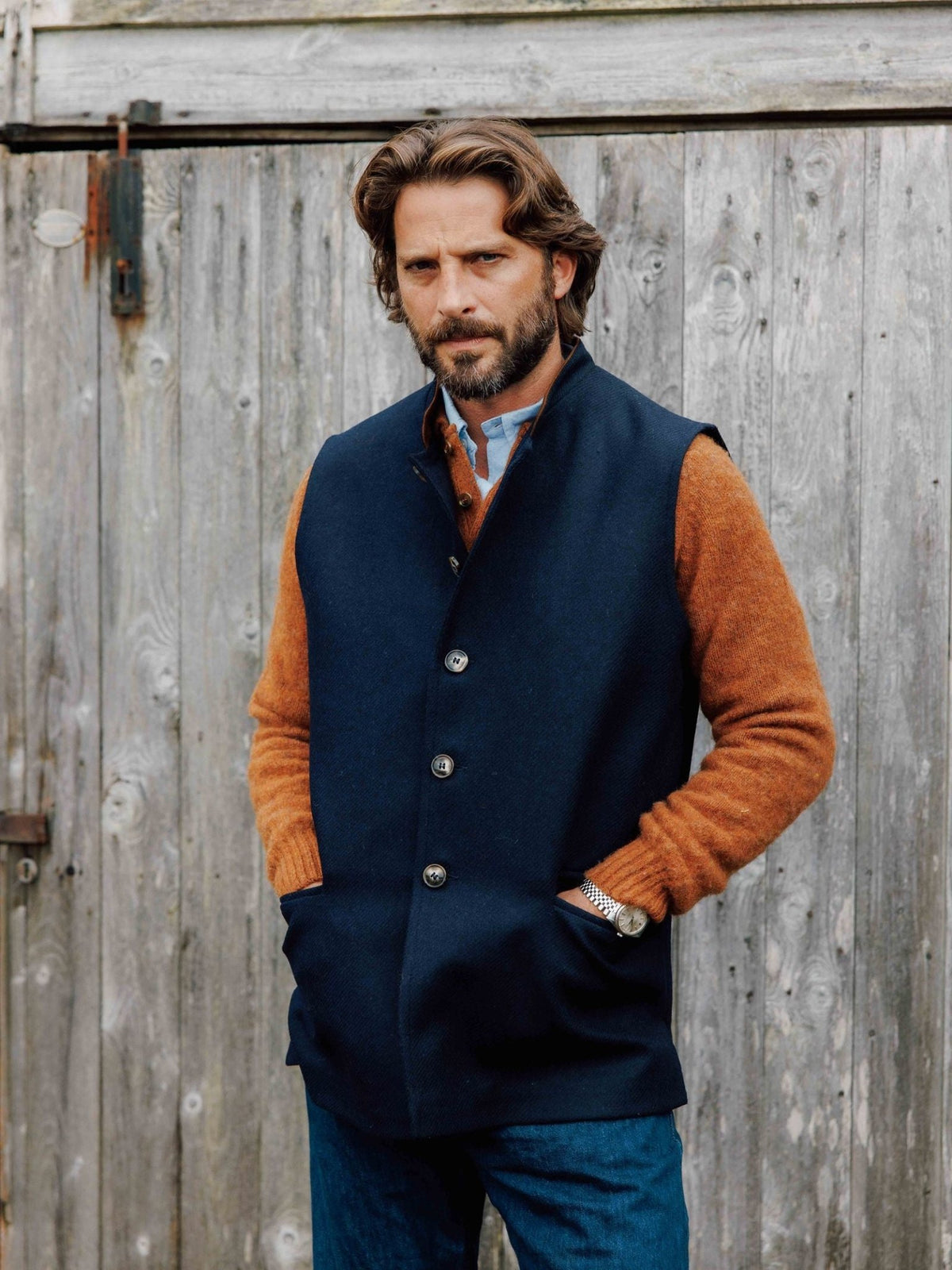 A man wearing a navy blue Campbell’s of Beauly Tweed Nehru gilet over a mustard-colored sweater.