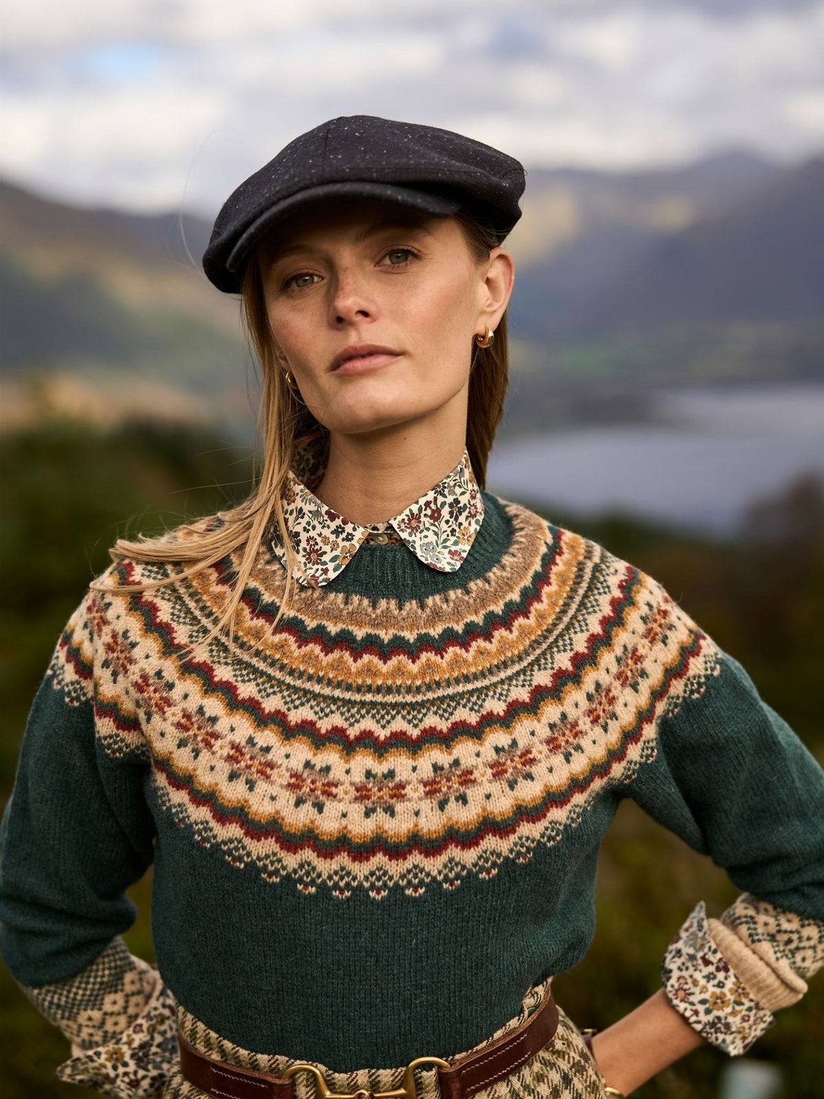 A person wearing a dark grey Unisex Affric Cap from Campbell’s of Beauly and a green patterned yoke sweater over a floral collared shirt, reflecting traditional British styles.