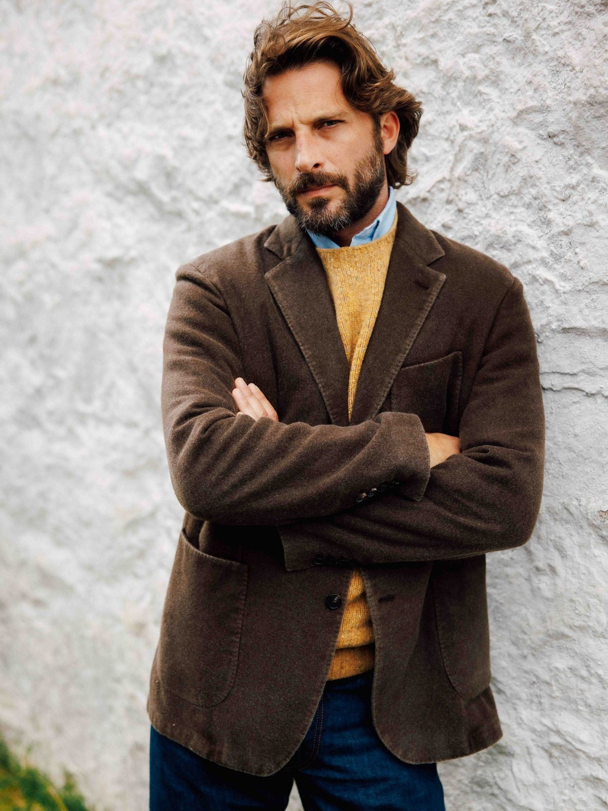A bearded man stands with arms crossed, wearing a brown woven Campbell’s of Beauly Washed Cashmere Jacket over a yellow sweater and a light blue collared shirt.