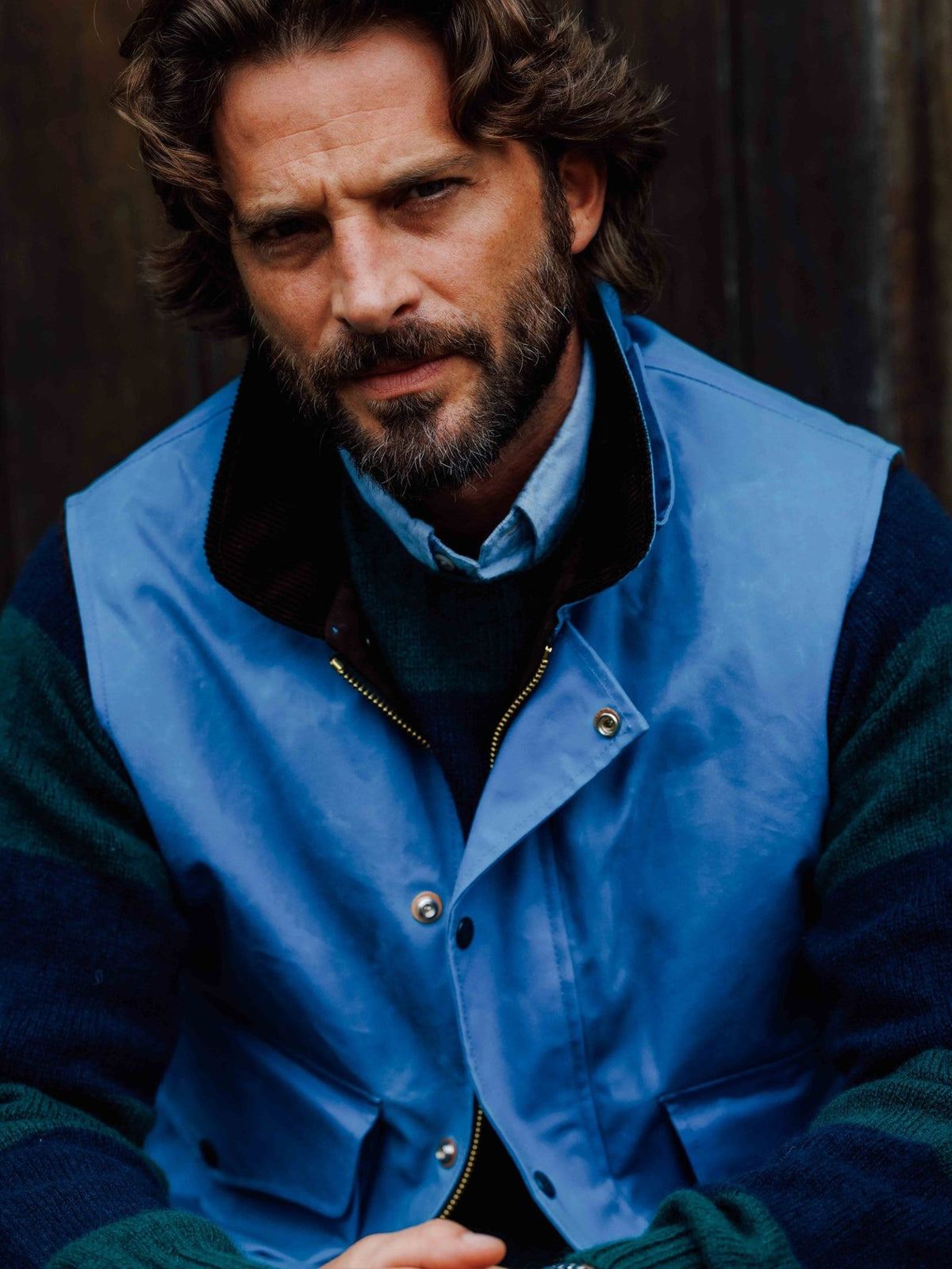 A man wears a blue Wax Nehru Gilet with a stand-up collar over a striped sweater and light blue shirt, showcasing Italian craftsmanship.