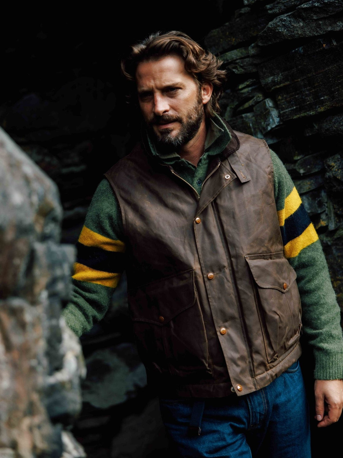 A man wearing a brown waxed-cotton Campbell’s of Beauly Wax Nehru Gilet over a green, yellow, and navy striped sweater.