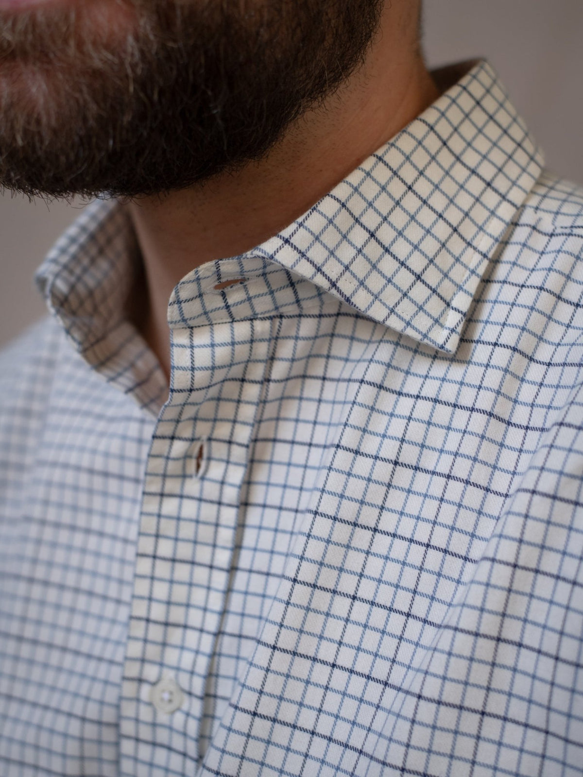 Close-up of a person wearing the Campbell’s of Beauly Windowpane Shirt—a white brushed cotton shirt featuring a blue grid pattern. The image highlights the collar, upper chest, and part of the person’s bearded jawline.