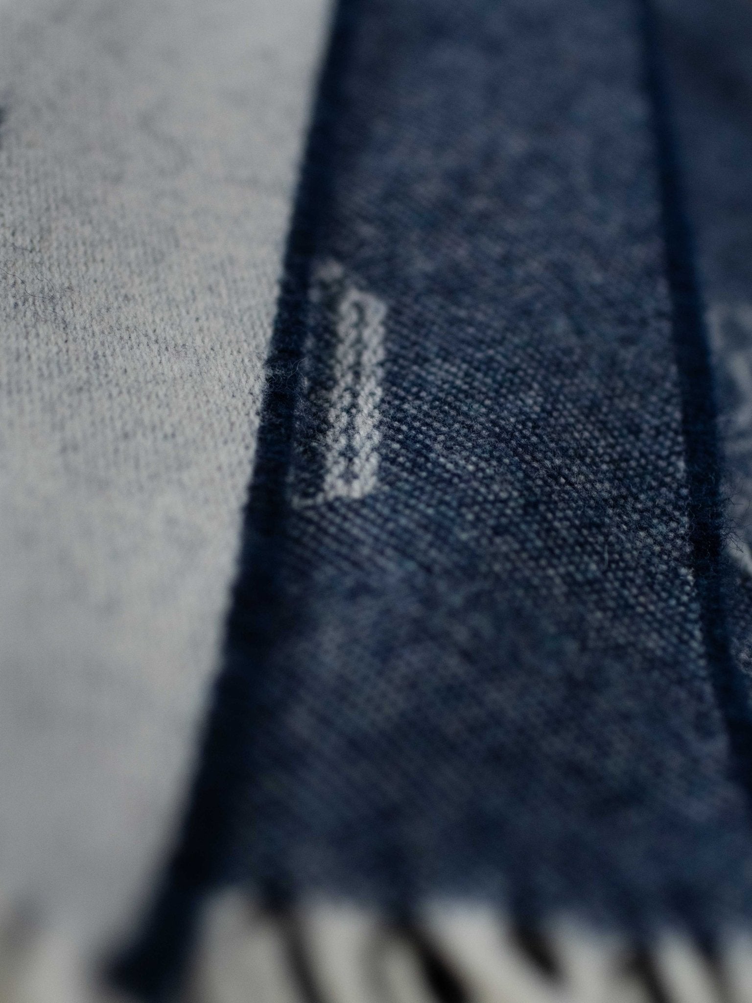 A close-up of the Land Rover Defender Jacquard Throw by Campbell's of Beauly, showing its soft woven British wool, alternating light and dark blue stripes, fringed edges, and detailed texture.