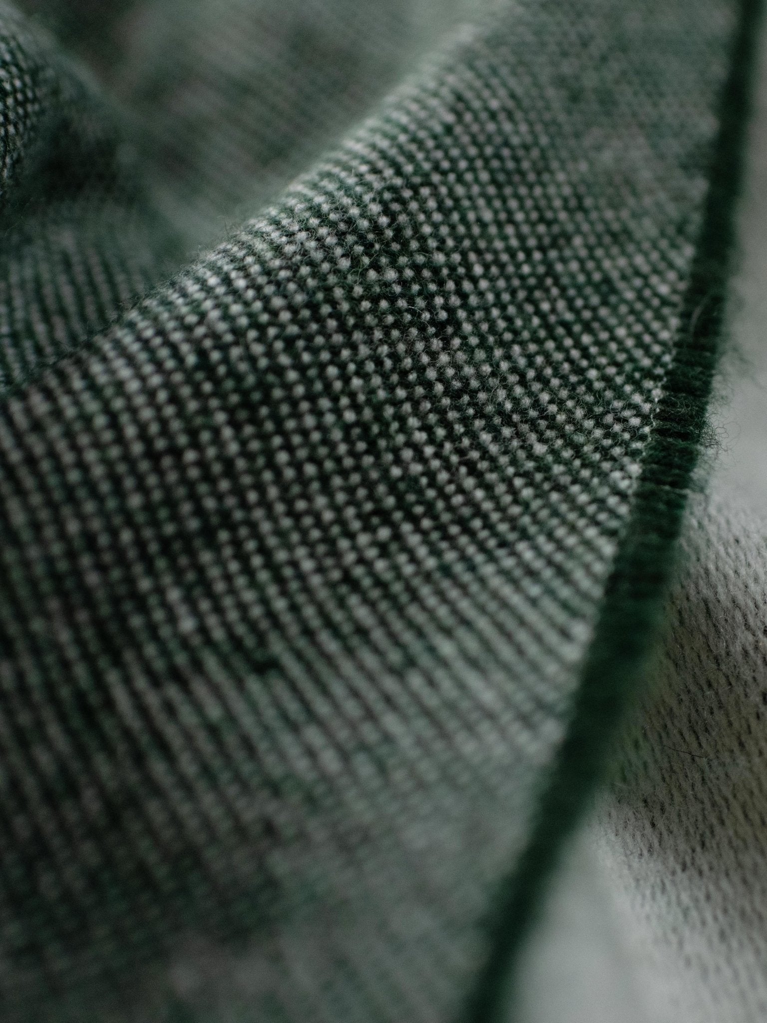 Close-up of textured dark green fabric with visible woven threads, showcasing the detail and softness of the Campbell's of Beauly Land Rover Defender Jacquard Throw—ideal as a British wool blanket or stylish Defender accessory.