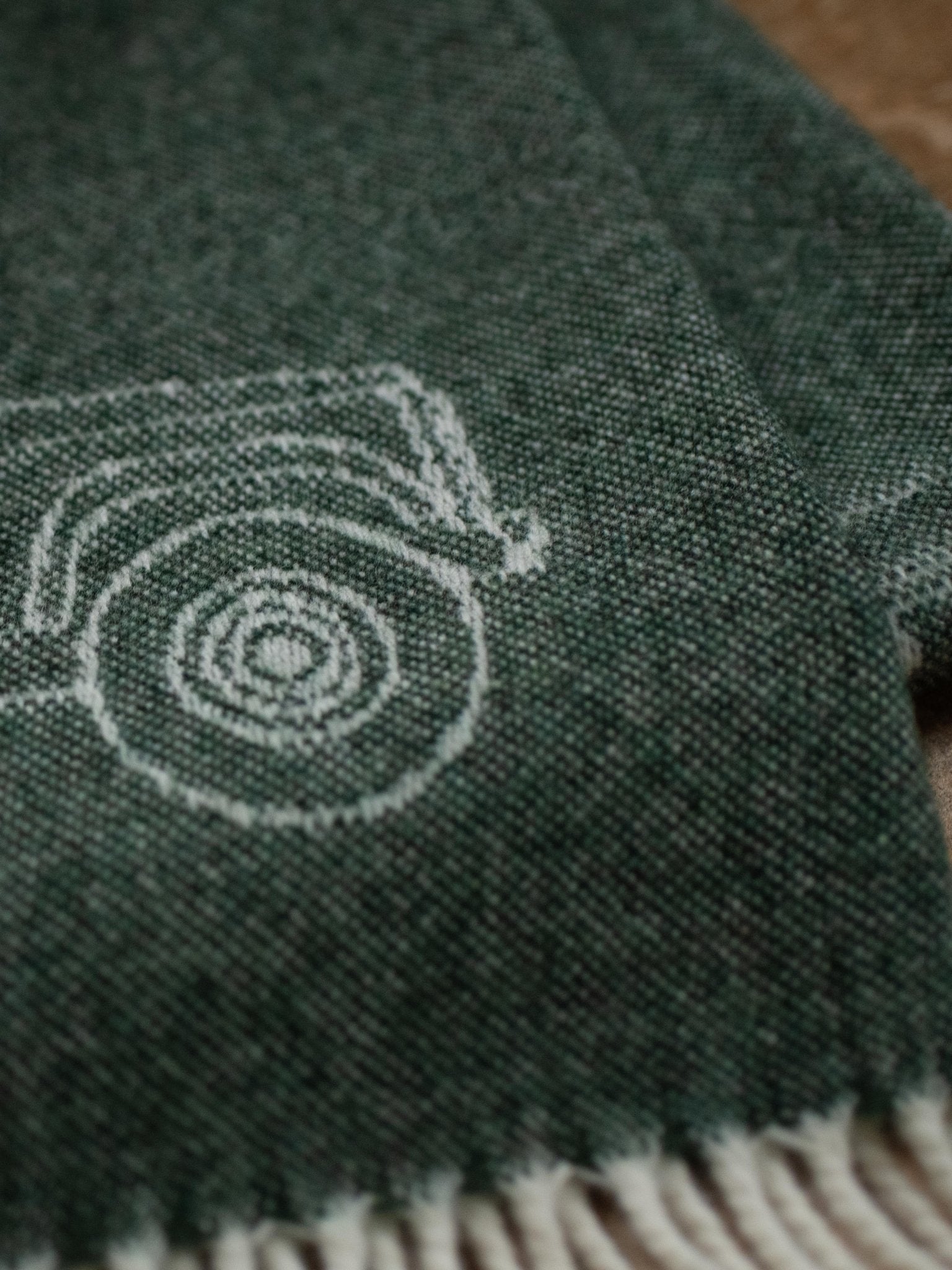 A close-up of the Campbell's of Beauly Land Rover Defender Jacquard Throw, a green wool blanket with a white outline of a vehicle tire and wheel arch, finished with fringed edges.